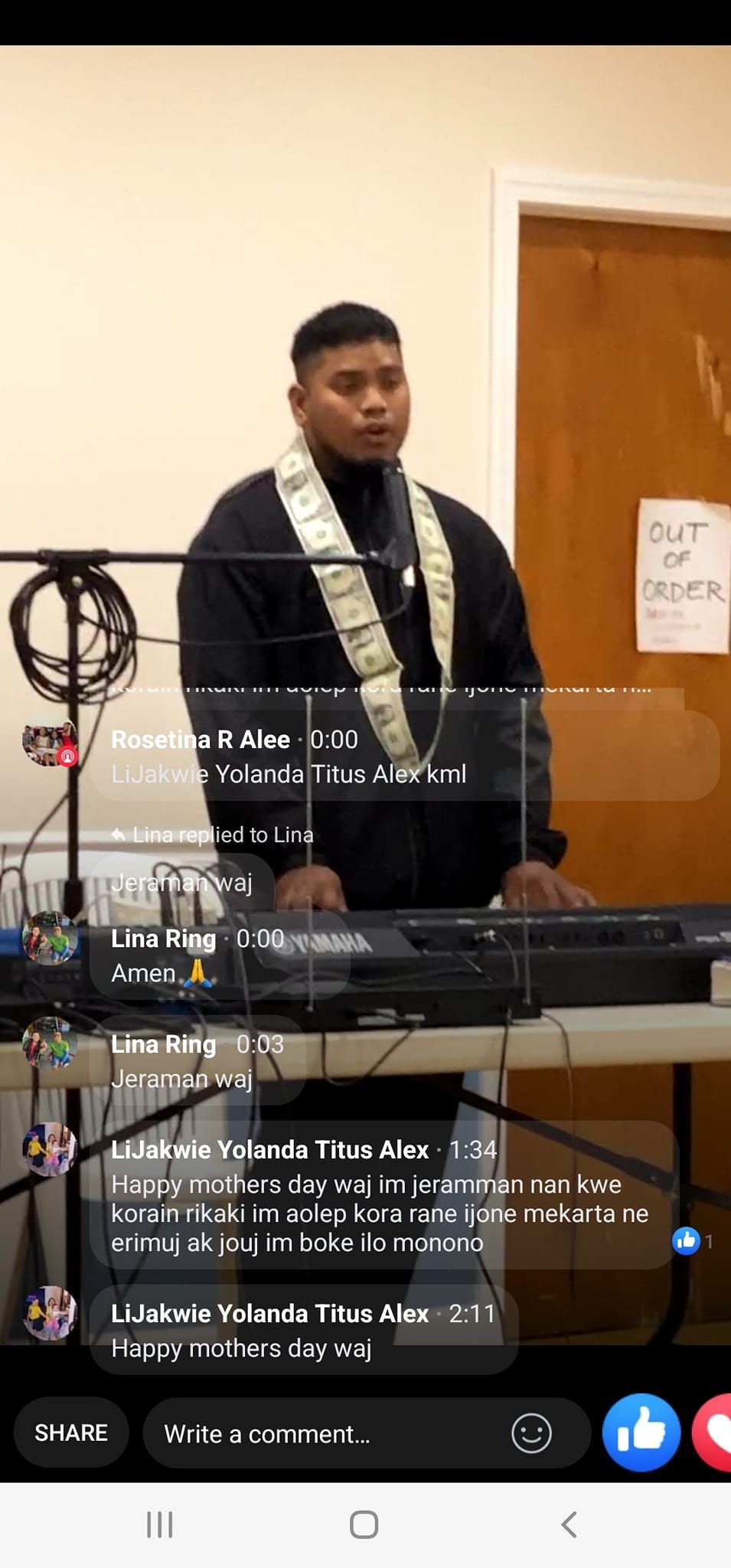 Man playing a keyboard at an event, wearing a lei.