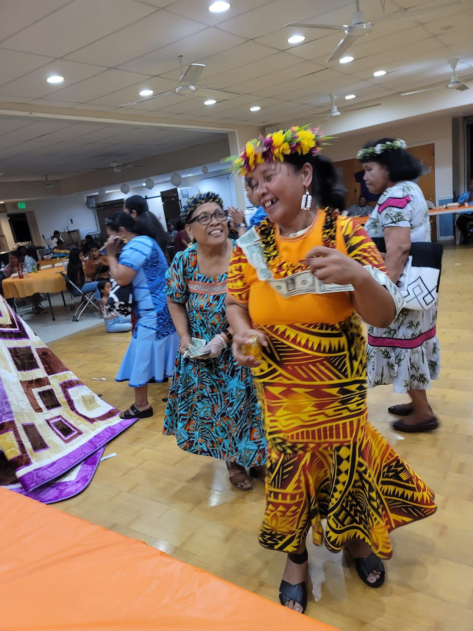 People dancing at an event. Woman in yellow dress with flower crown, money in hand, laughing.