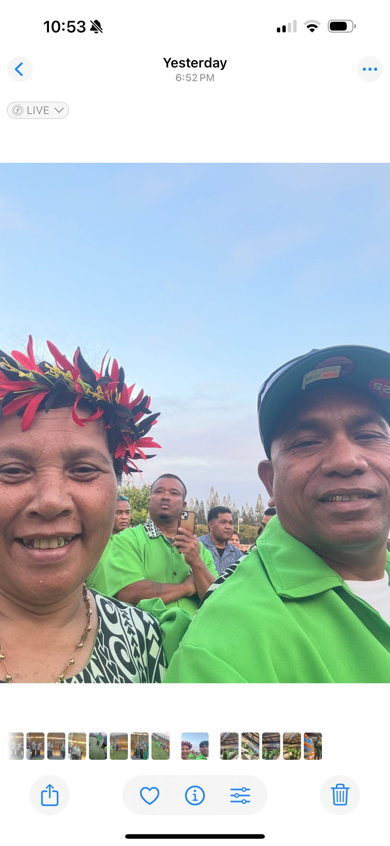 Two people smile at the camera. A woman with a floral headdress smiles next to a man in a green shirt and cap.