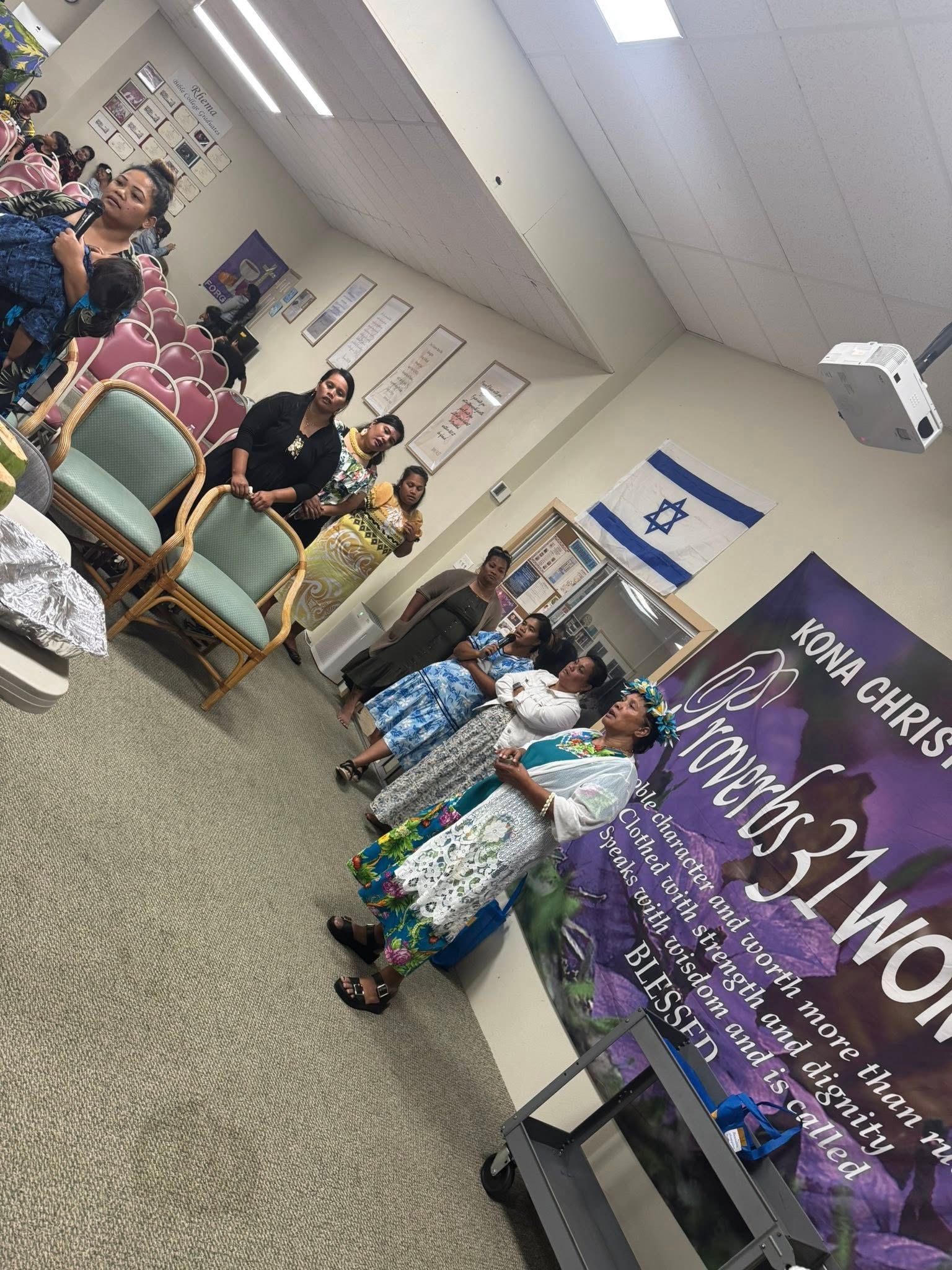 Group of women at a Kona Christian event; purple banner, Israel flag, attendees dressed up.