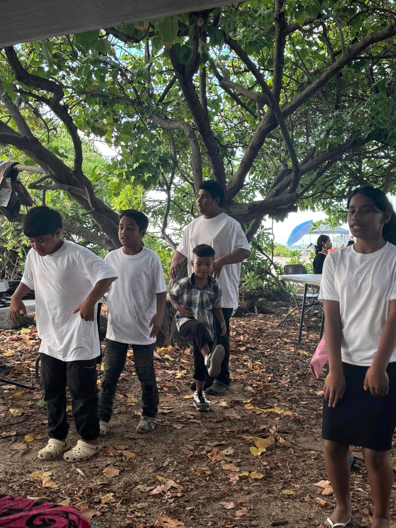 Five young people in white shirts, outdoors, pose under trees.