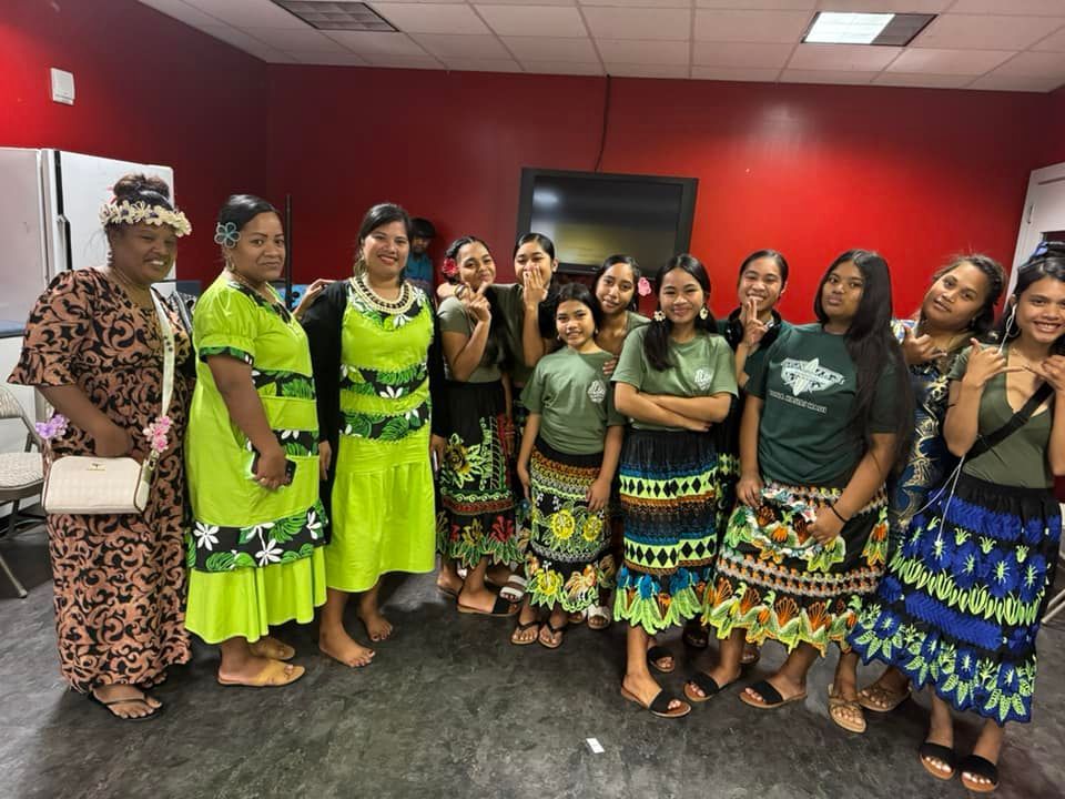 Group of women in colorful traditional attire, posing in a red-walled room.