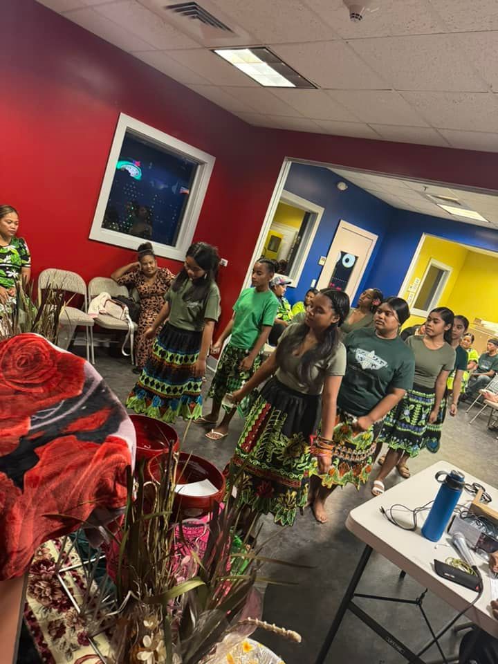 Group of women in colorful skirts and olive shirts, dancing indoors.