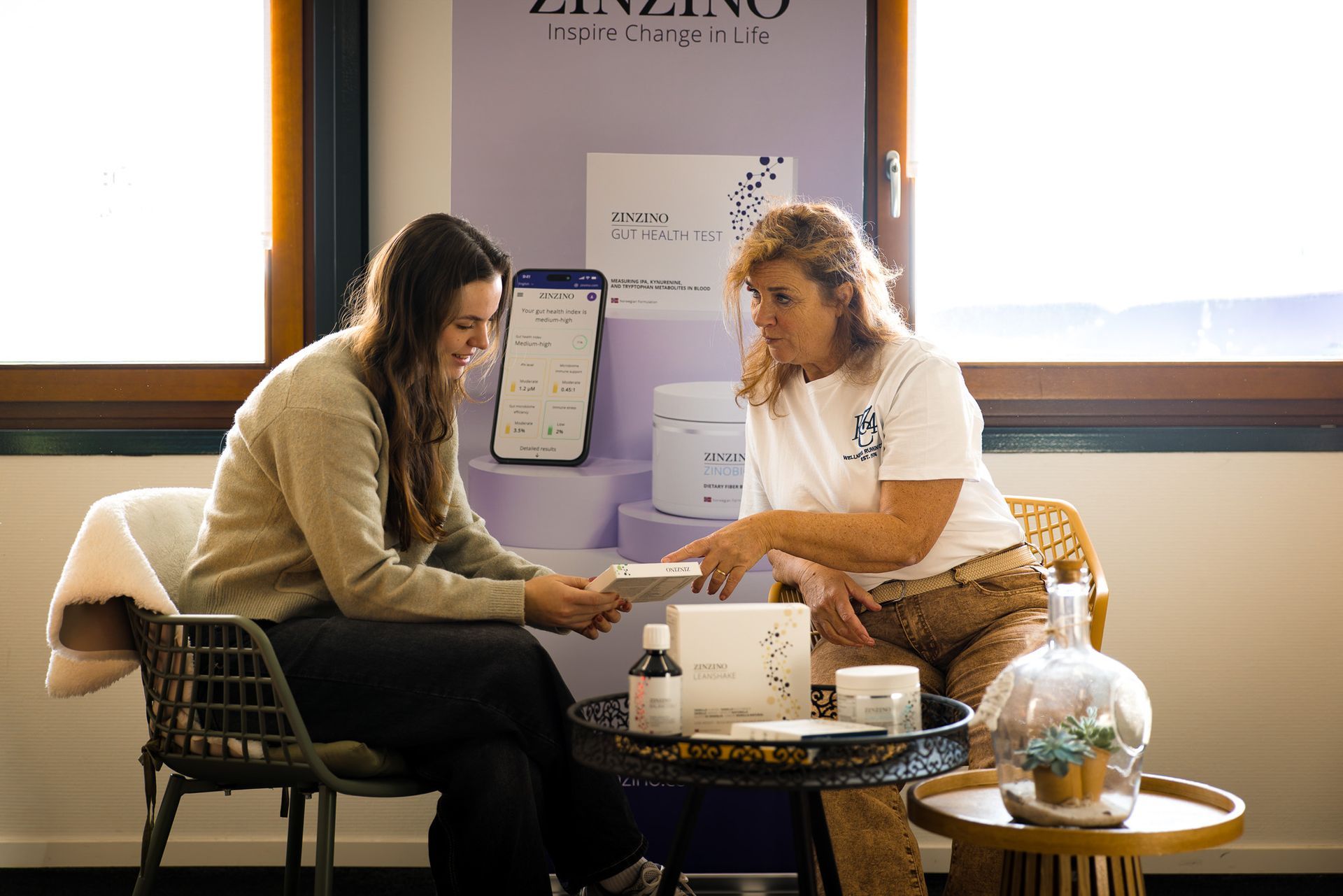 Twee vrouwen zitten aan een tafel en bespreken een product.