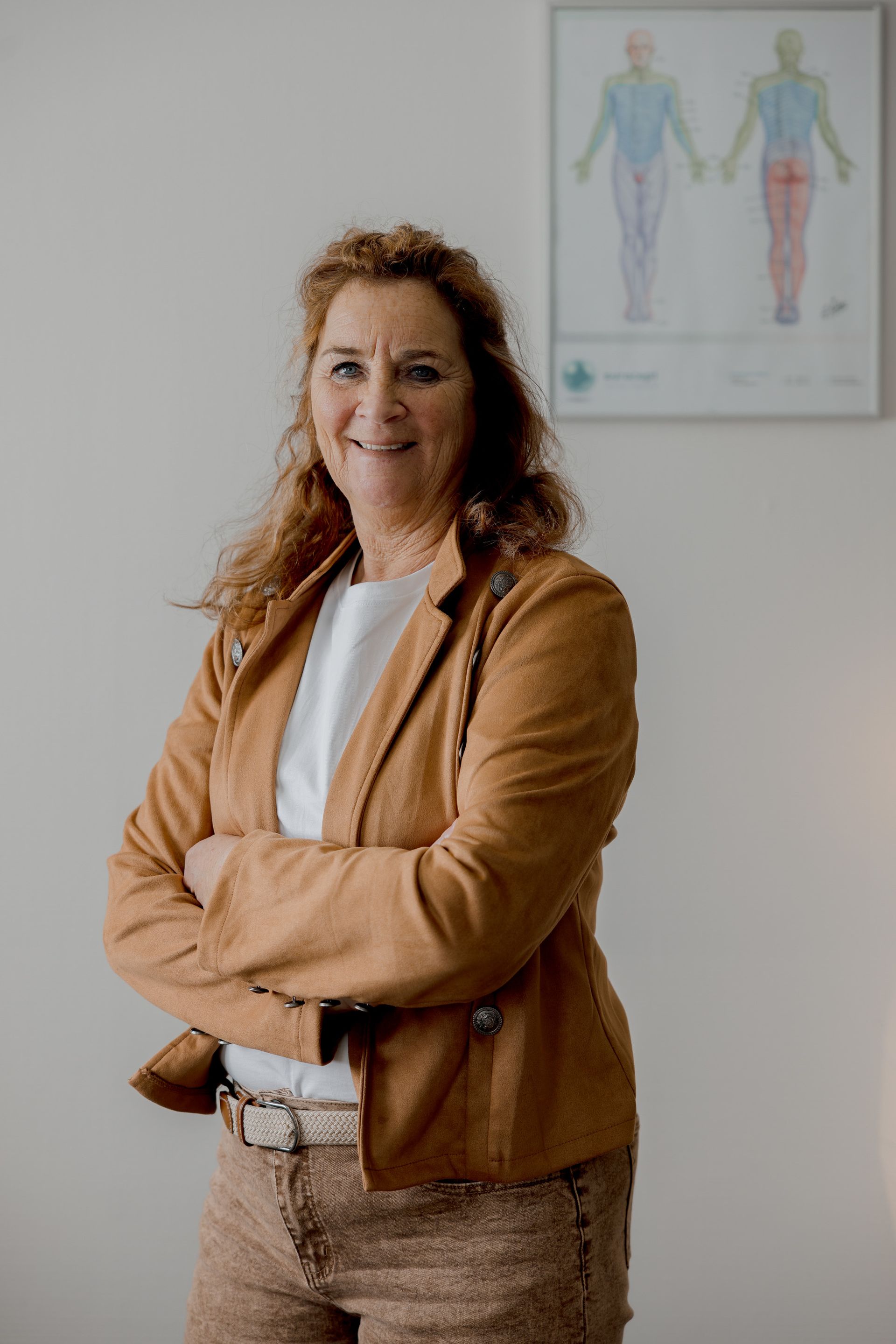 Vrouw in een bruine jas en een broek met patroon, armen over elkaar, glimlachend. Medisch dossier op de achtergrond.