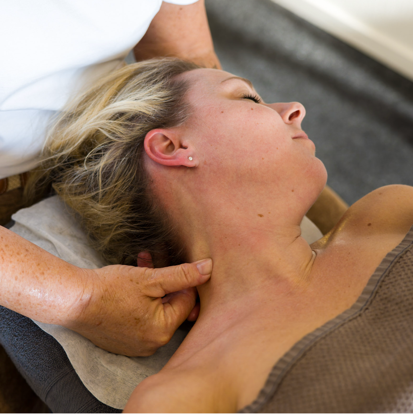 Person receiving neck massage; therapist's hand on client's neck, client's eyes closed, relaxation.