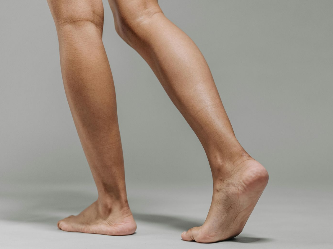 Vrouw in zwart shirt gebruikt een crosstrainer in een sportschool. Ze houdt zich vast aan de handgrepen.