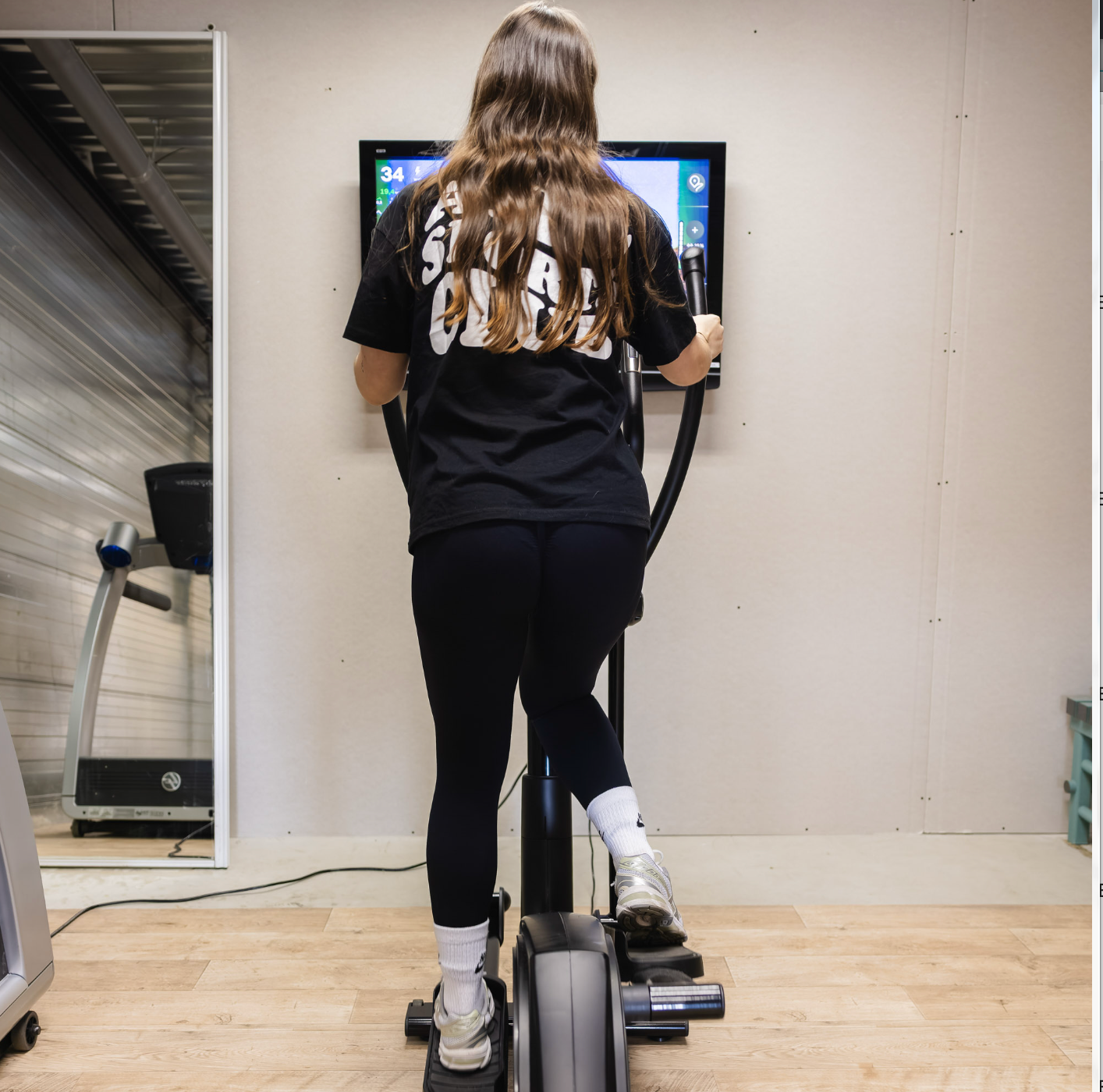 Vrouw op een crosstrainer, aan het sporten, gekleed in een zwart T-shirt en legging, in een sportschool.