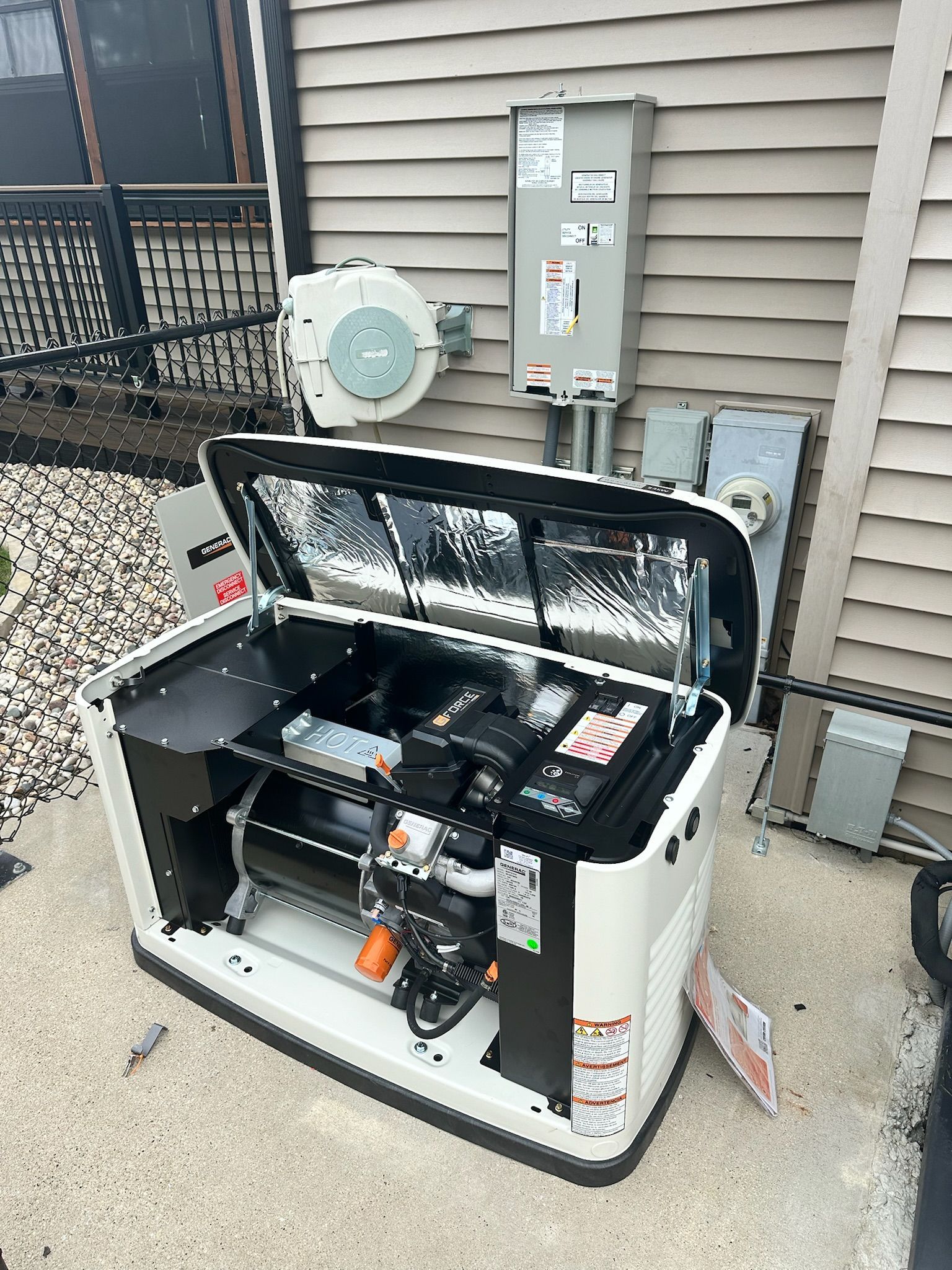 A generator installed in a persons backyard on their patio with the lid open.