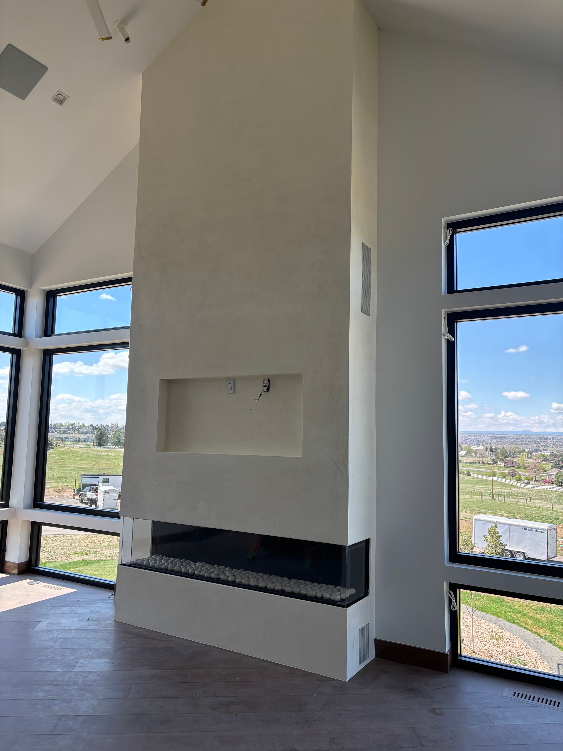 Tall, white fireplace in a modern living room with floor-to-ceiling windows and a view of the outdoors.