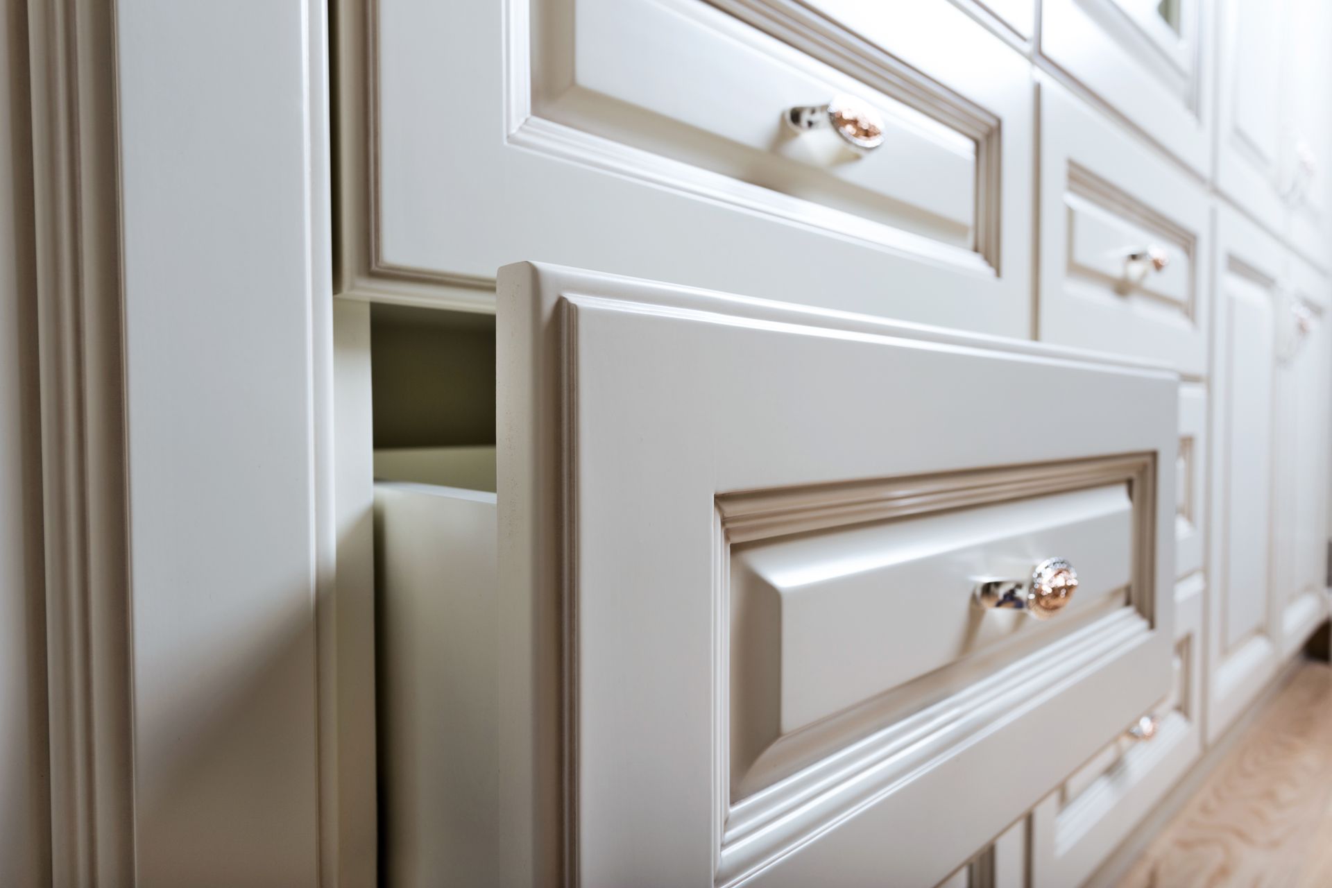 White kitchen drawers with ornate details and crystal knobs.