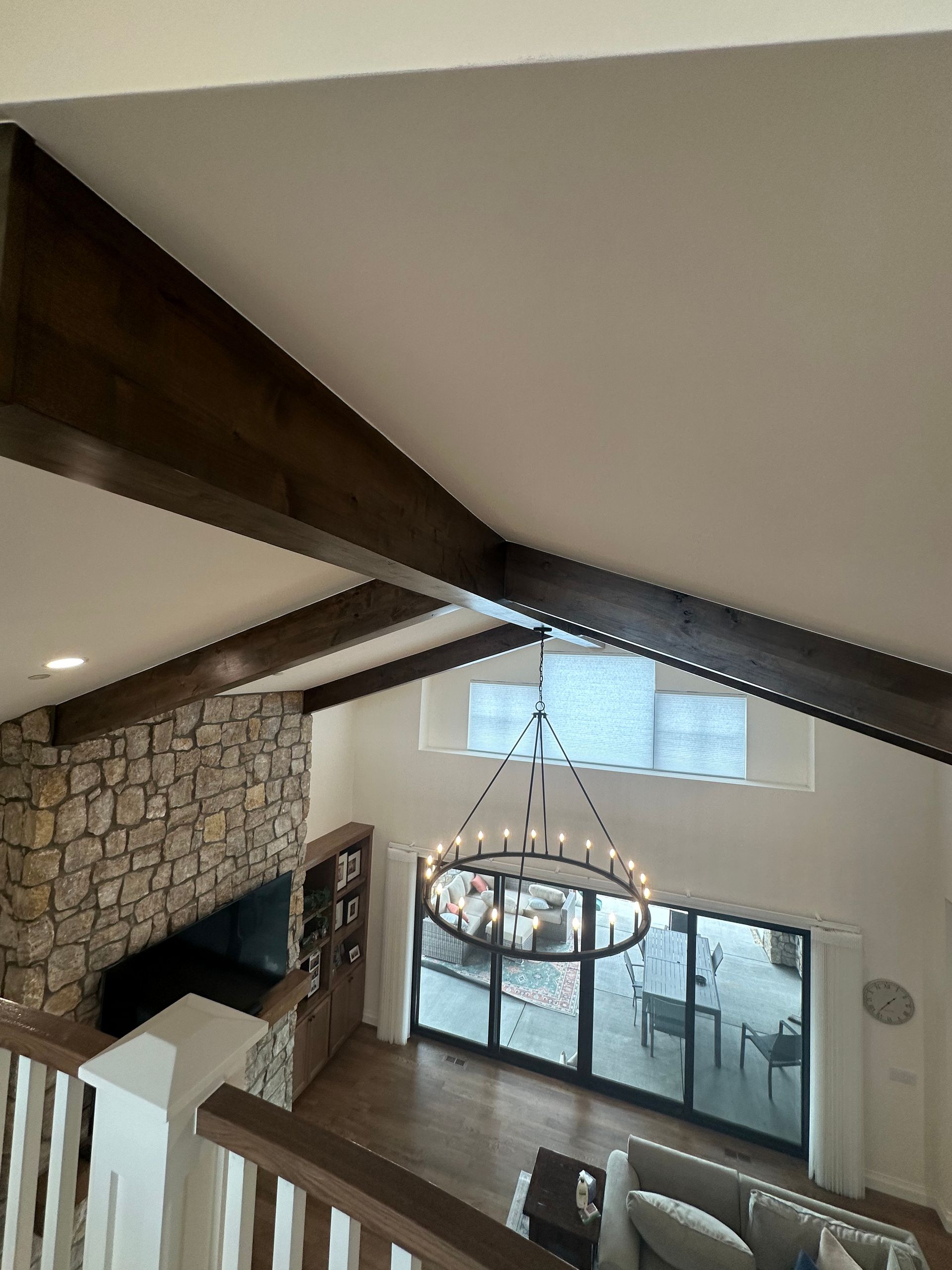High-angle view of a living room with exposed wooden beams, stone fireplace, and large windows.
