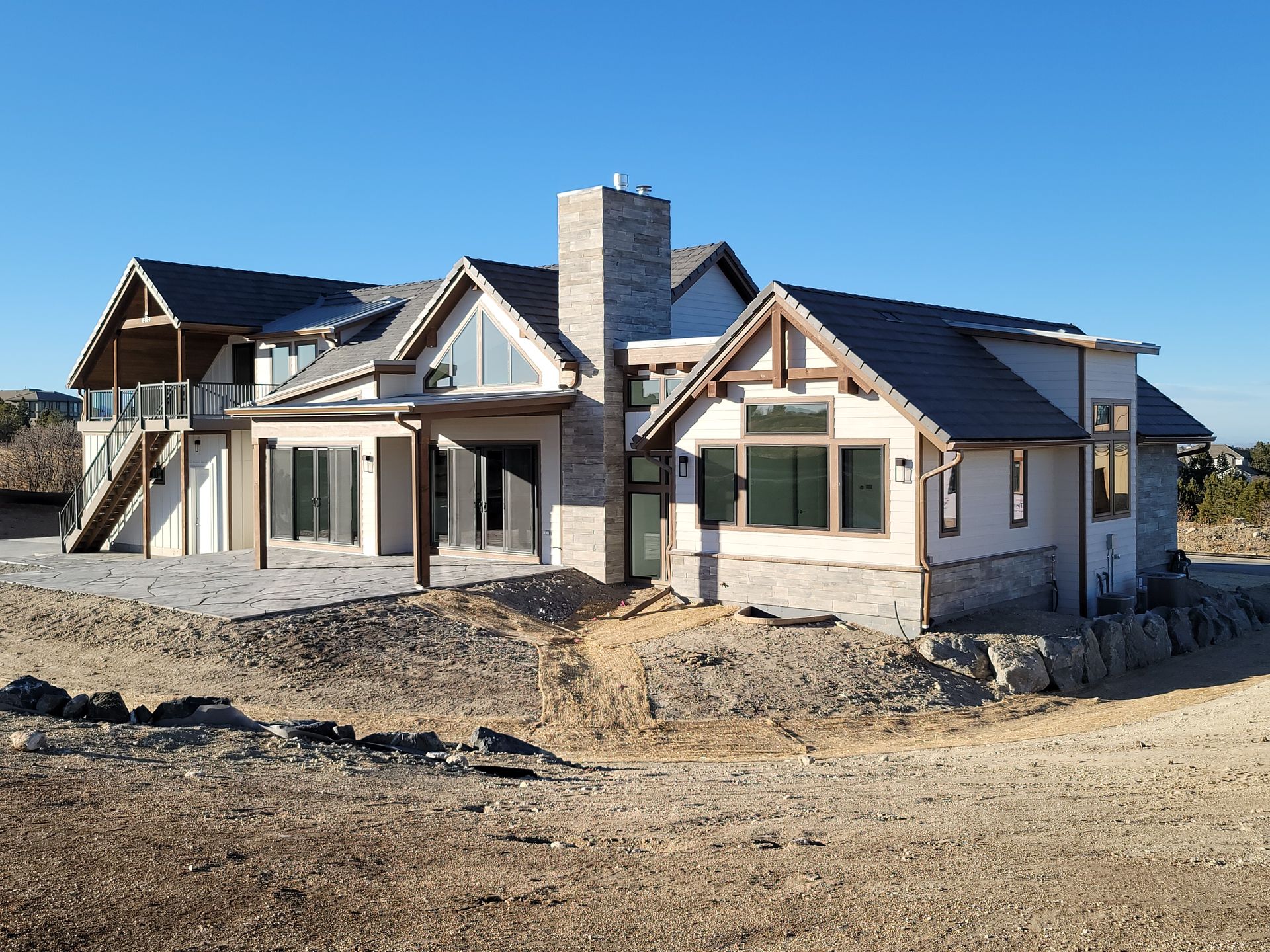 A modern, light-colored house under construction on a dirt lot with a blue sky.