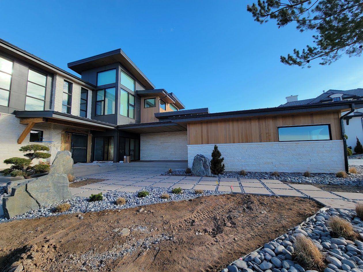 Modern house exterior with brick, wood siding, large windows, and a landscaped yard.