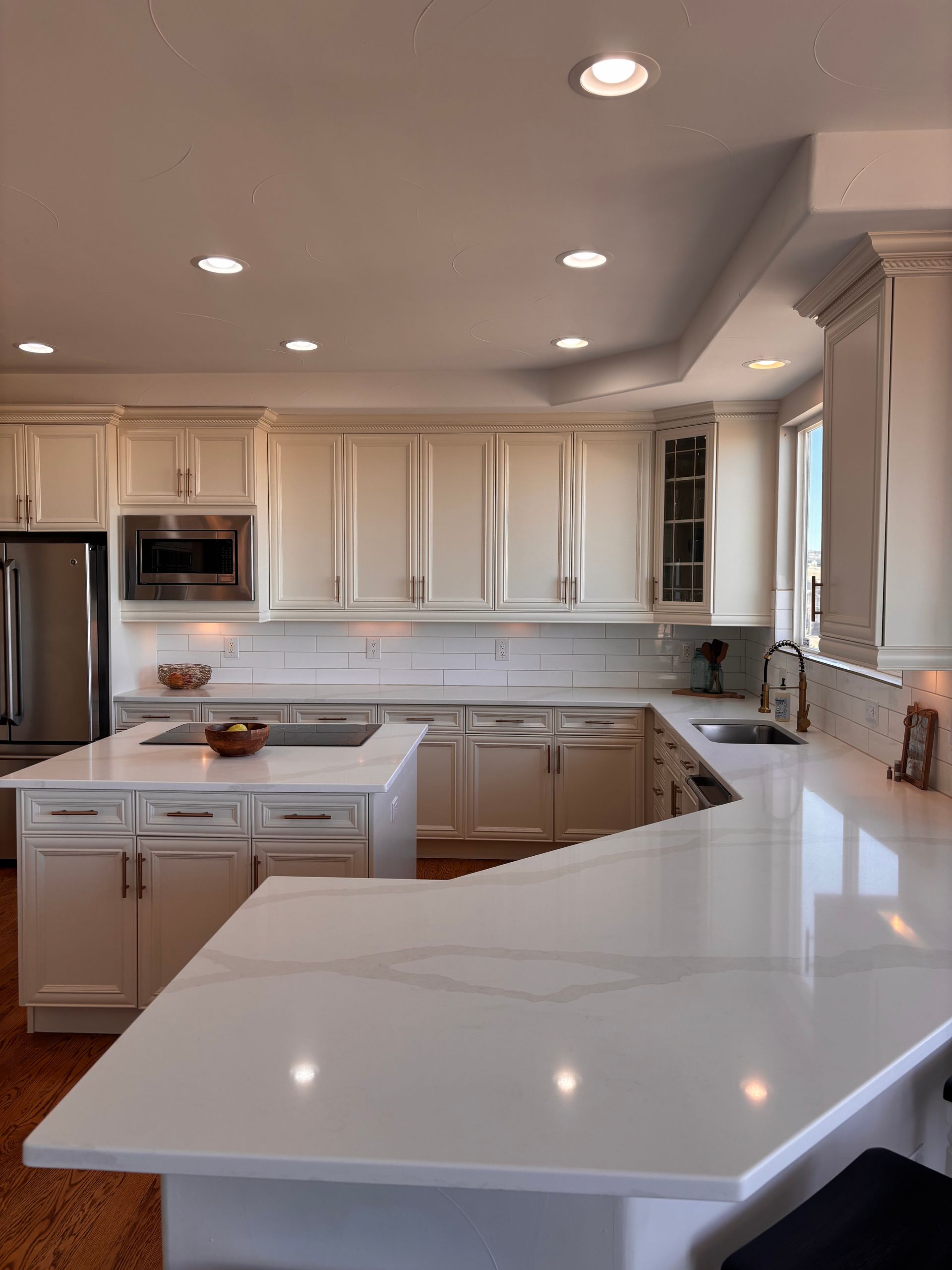 Bright white kitchen with a large island and countertops, stainless steel appliances, and recessed lighting.