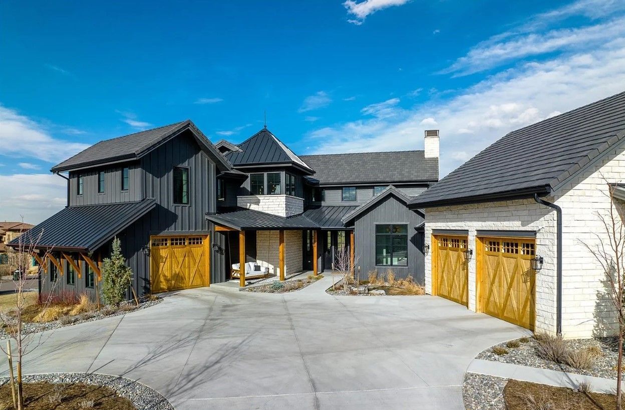 Modern two-story house with black siding and light wood garage doors on a sunny day.