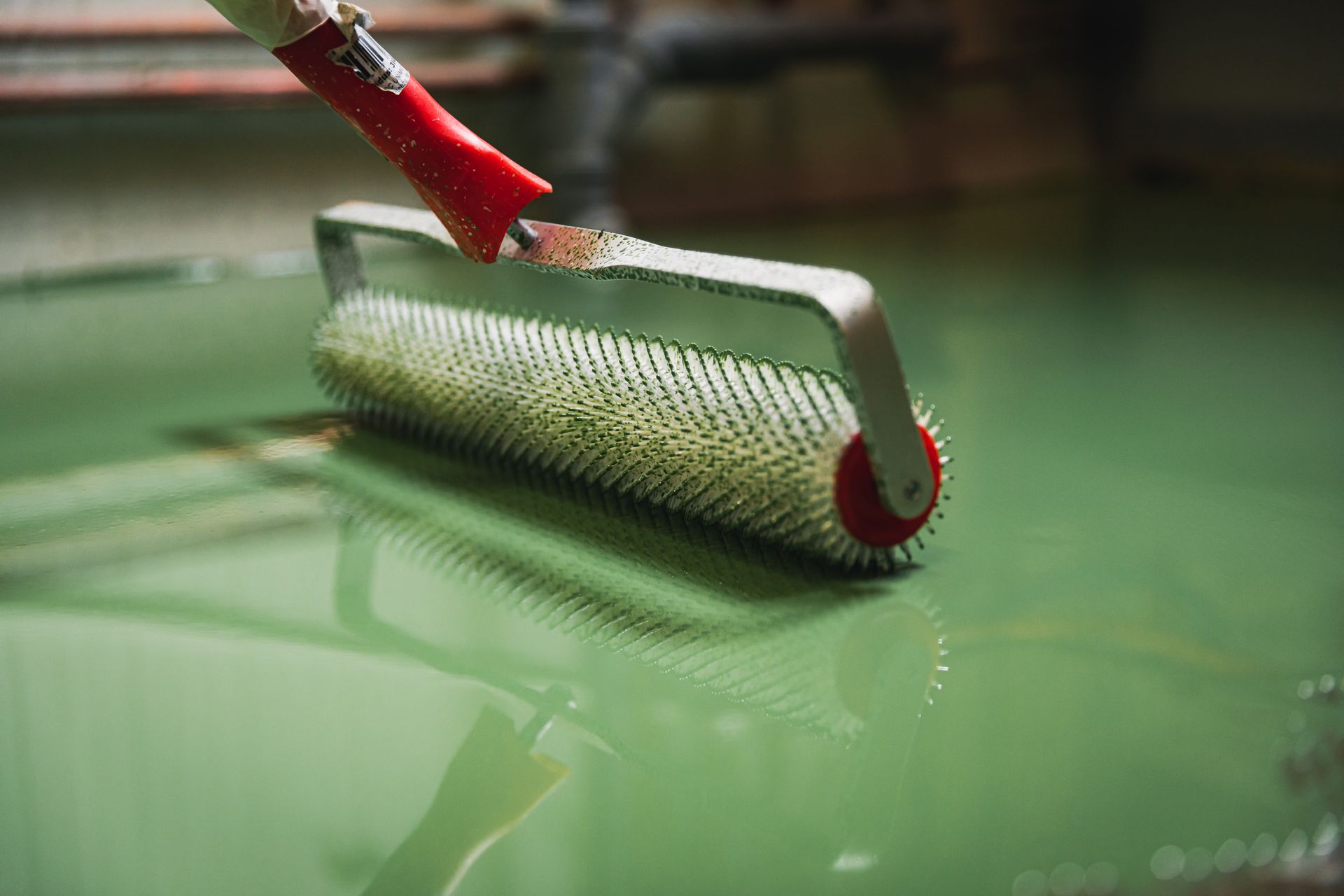 Green floor coating being smoothed with a spiked roller in an industrial setting.