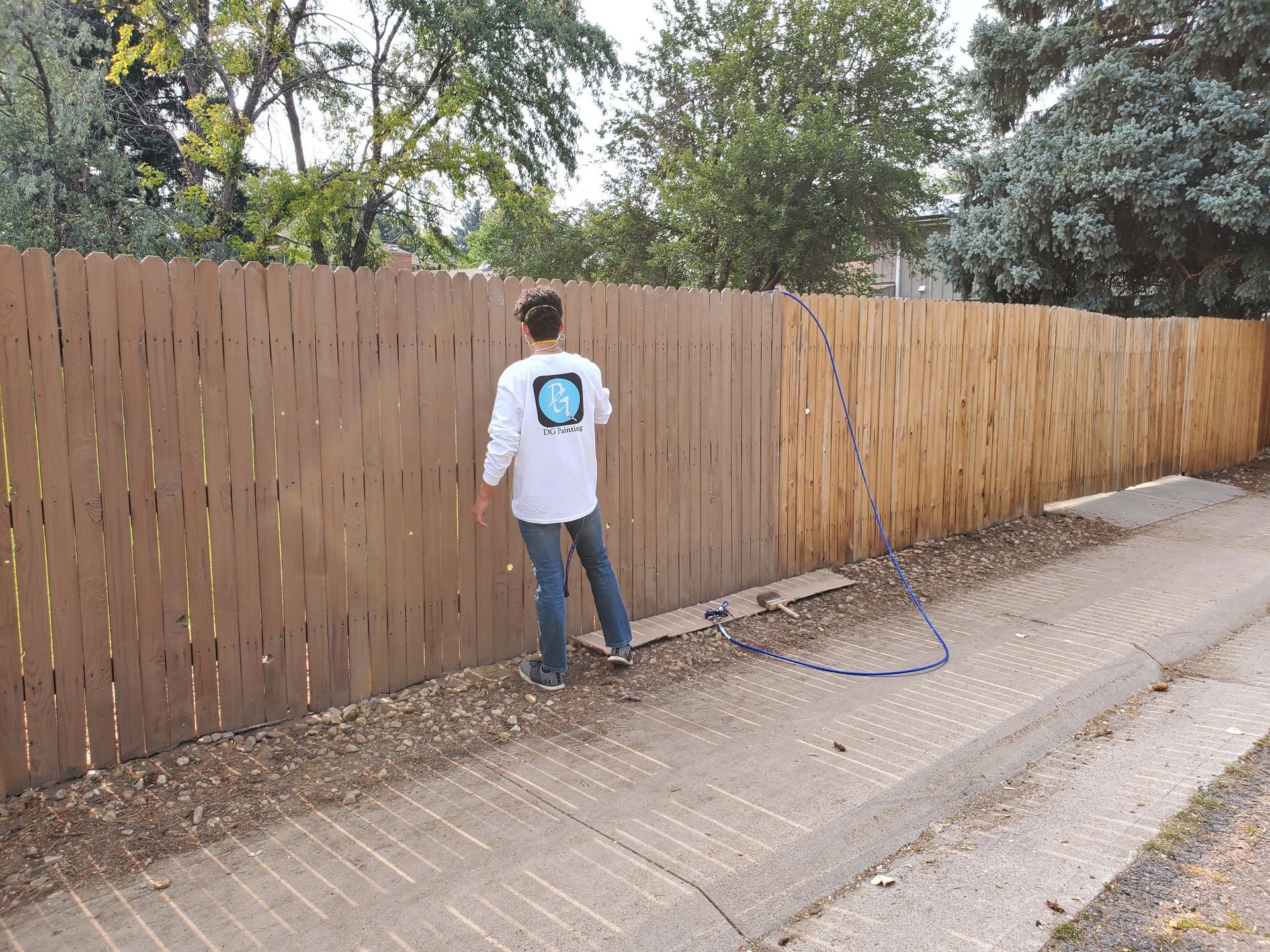 A man is standing next to a wooden fence with a hose attached to it.