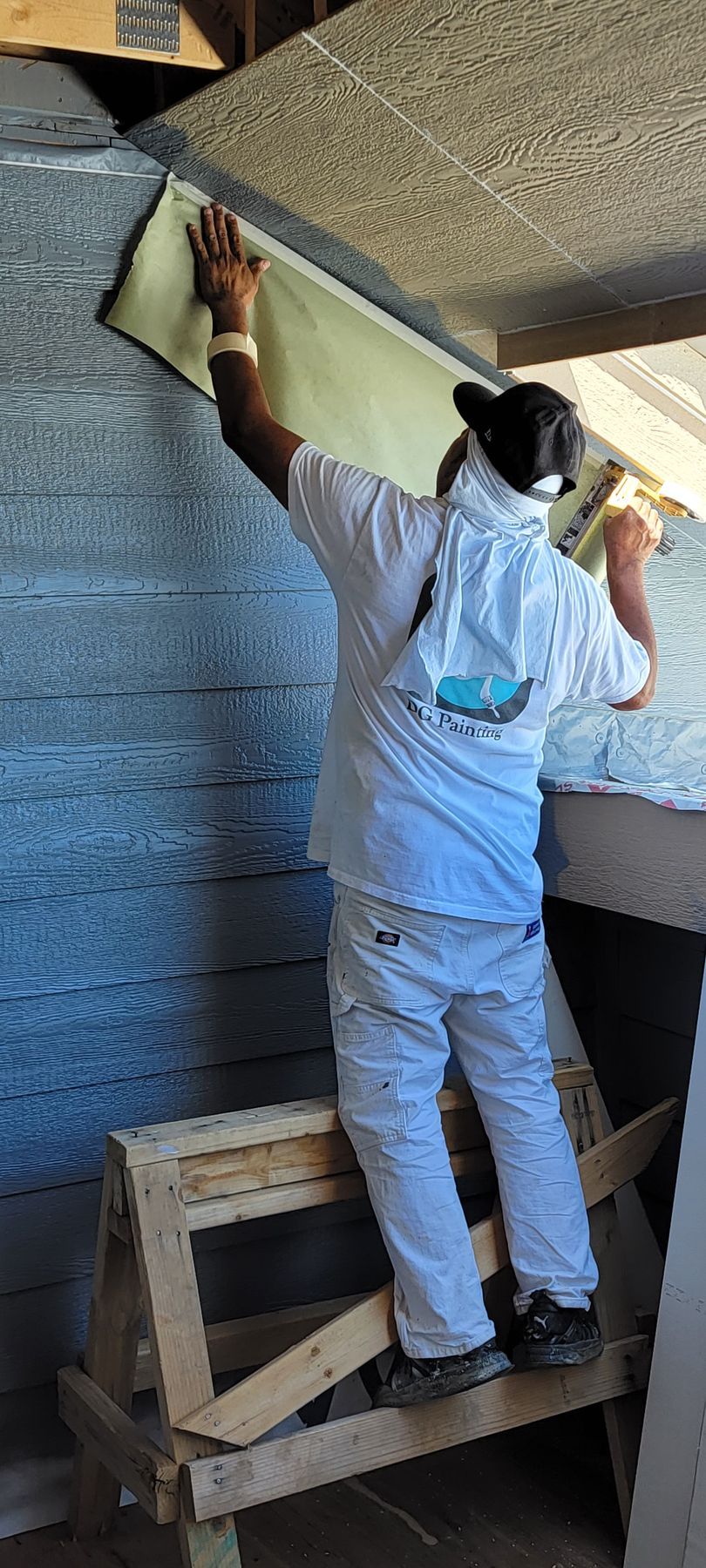 A man is standing on a wooden stool painting a wall.