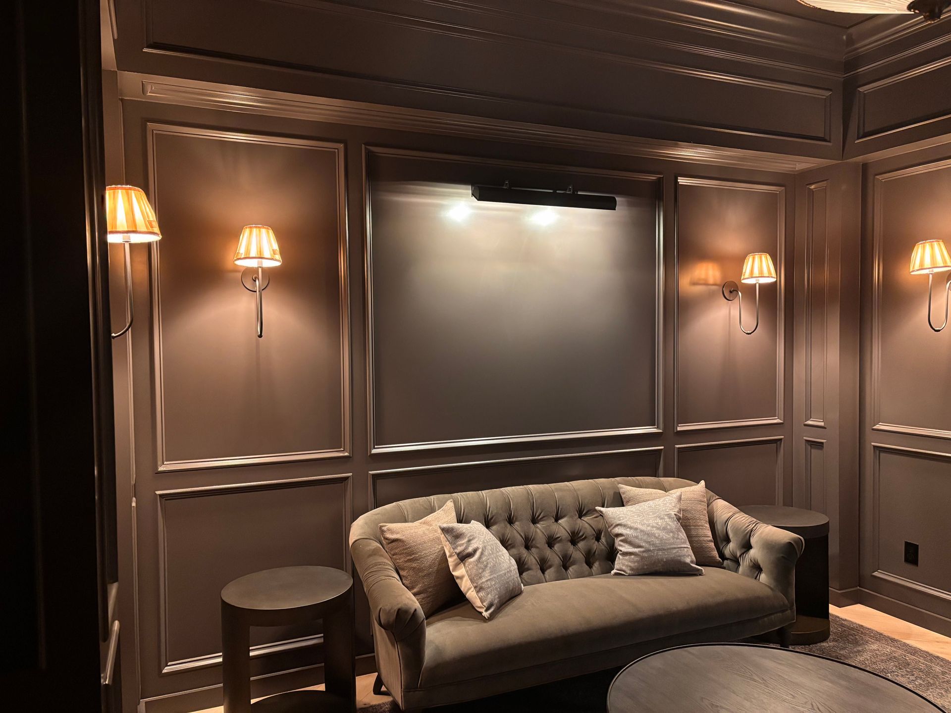 Cozy seating area with a button-tufted sofa, side tables, wall sconces, and a large, centered screen.
