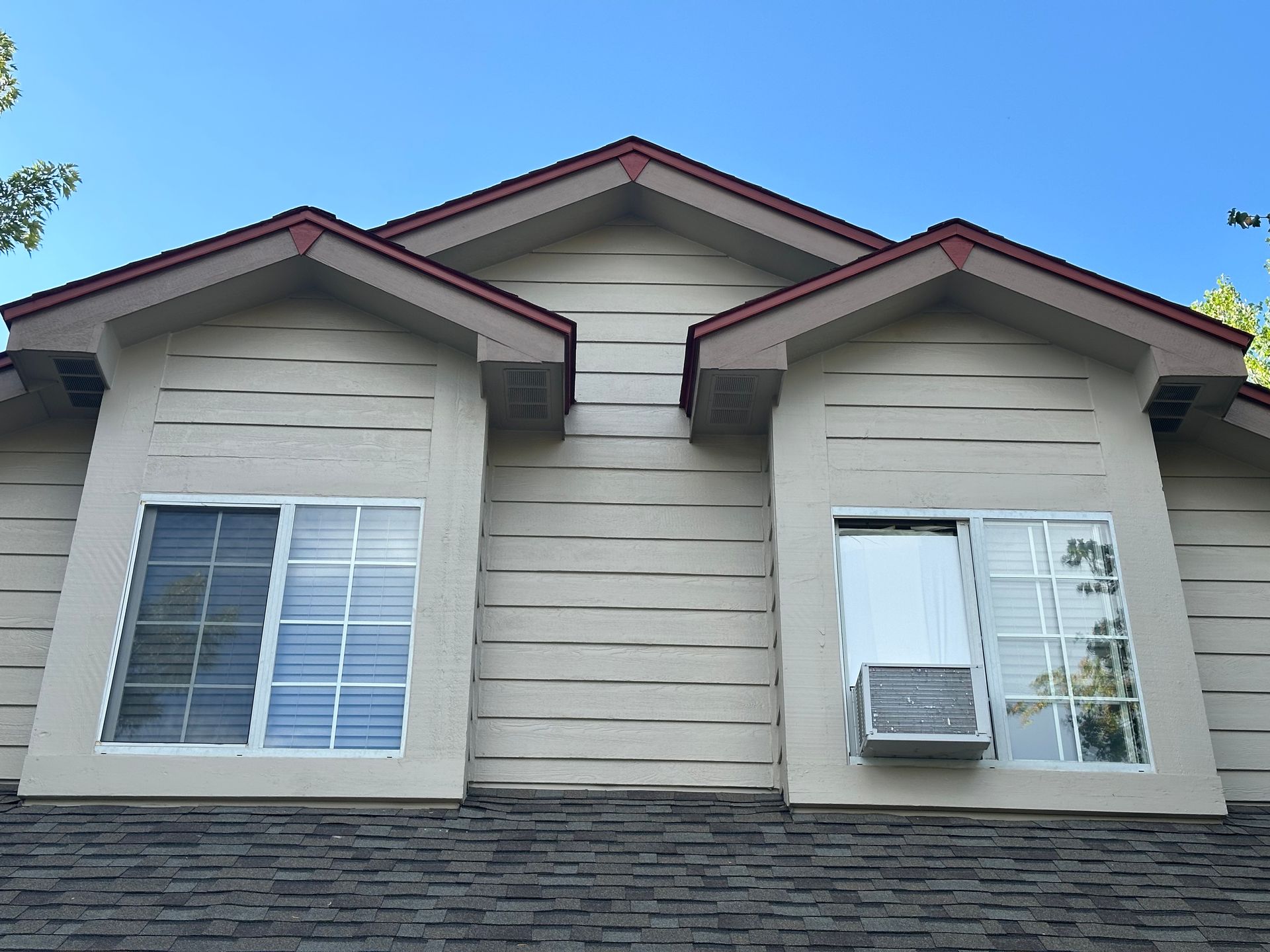 Exterior view of a two-story tan building with two gabled windows and a window air conditioning unit.