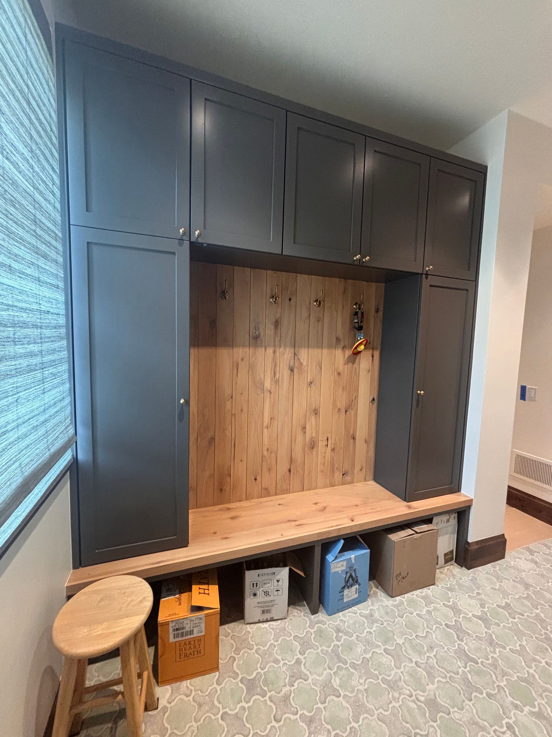 Gray built-in storage with a wooden bench and backboard. Some boxes and a stool sit below.