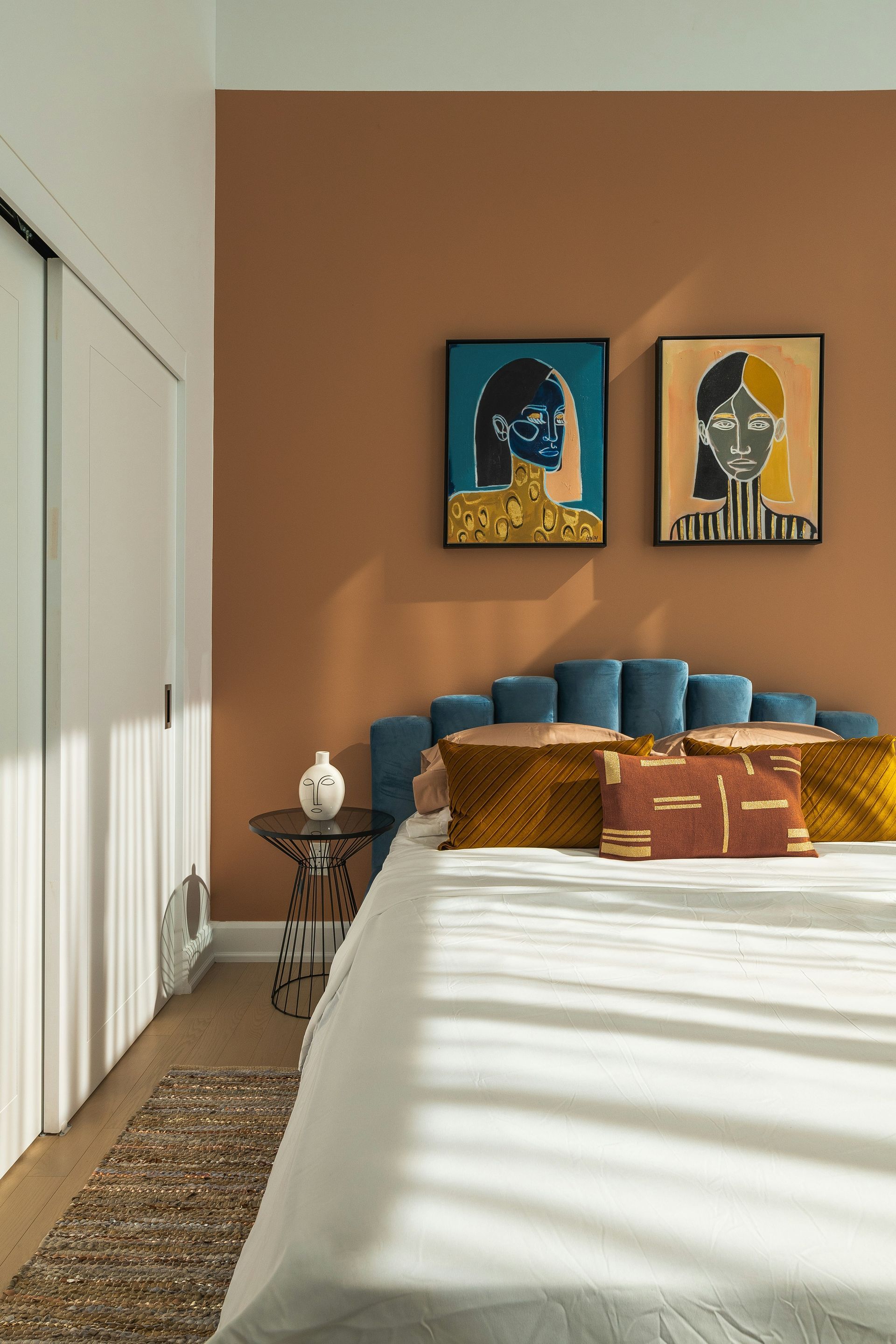 Bedroom with bed, blue headboard, brown accent wall, and artwork.