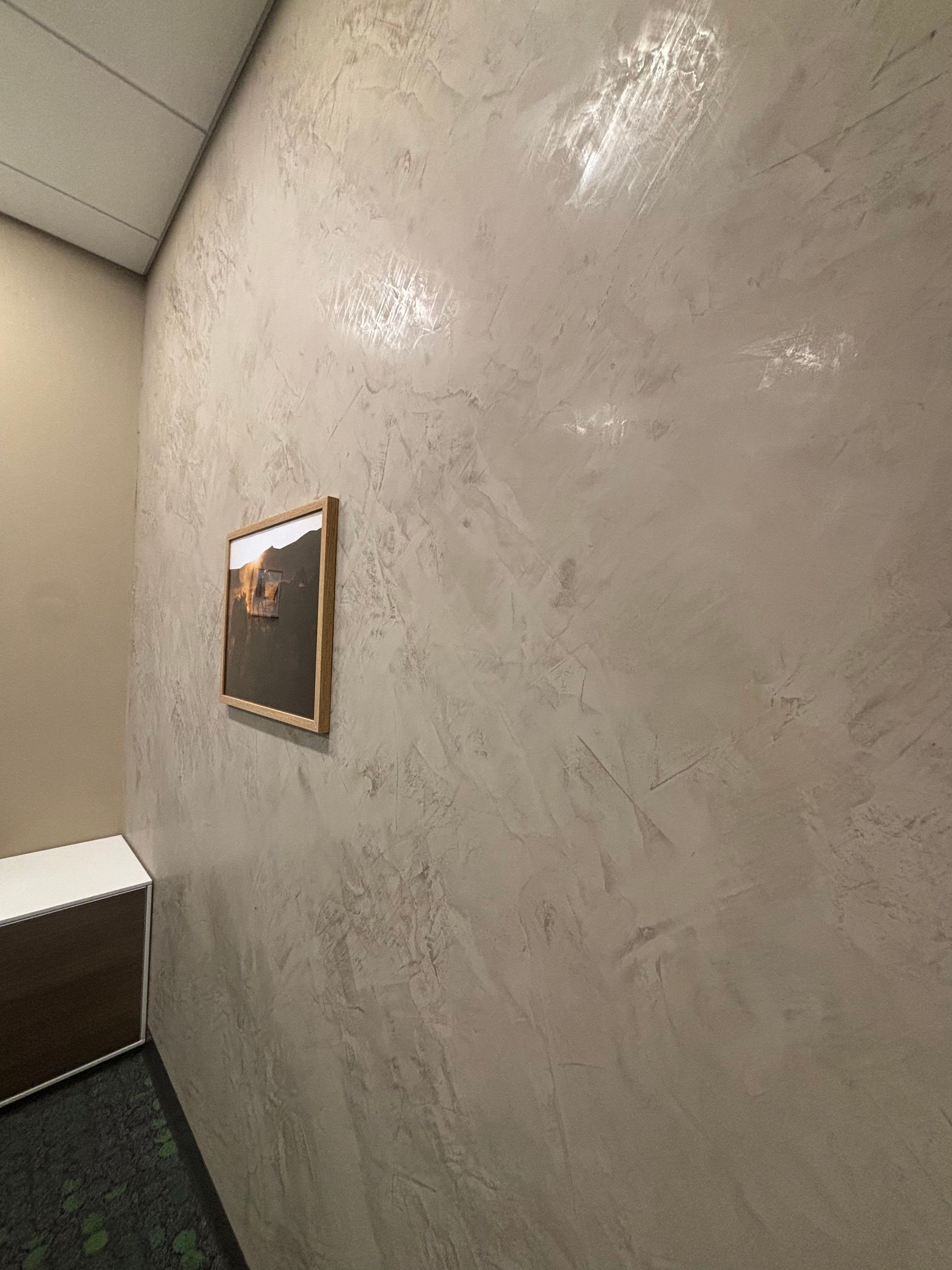 Wall with textured, light-colored finish and framed artwork; a small, dark cabinet is visible.