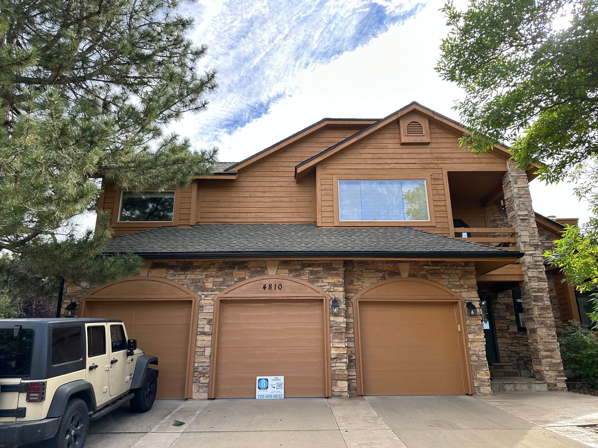 Two-story brown house with stone accents, three-car garage, and a tan Jeep parked outside.