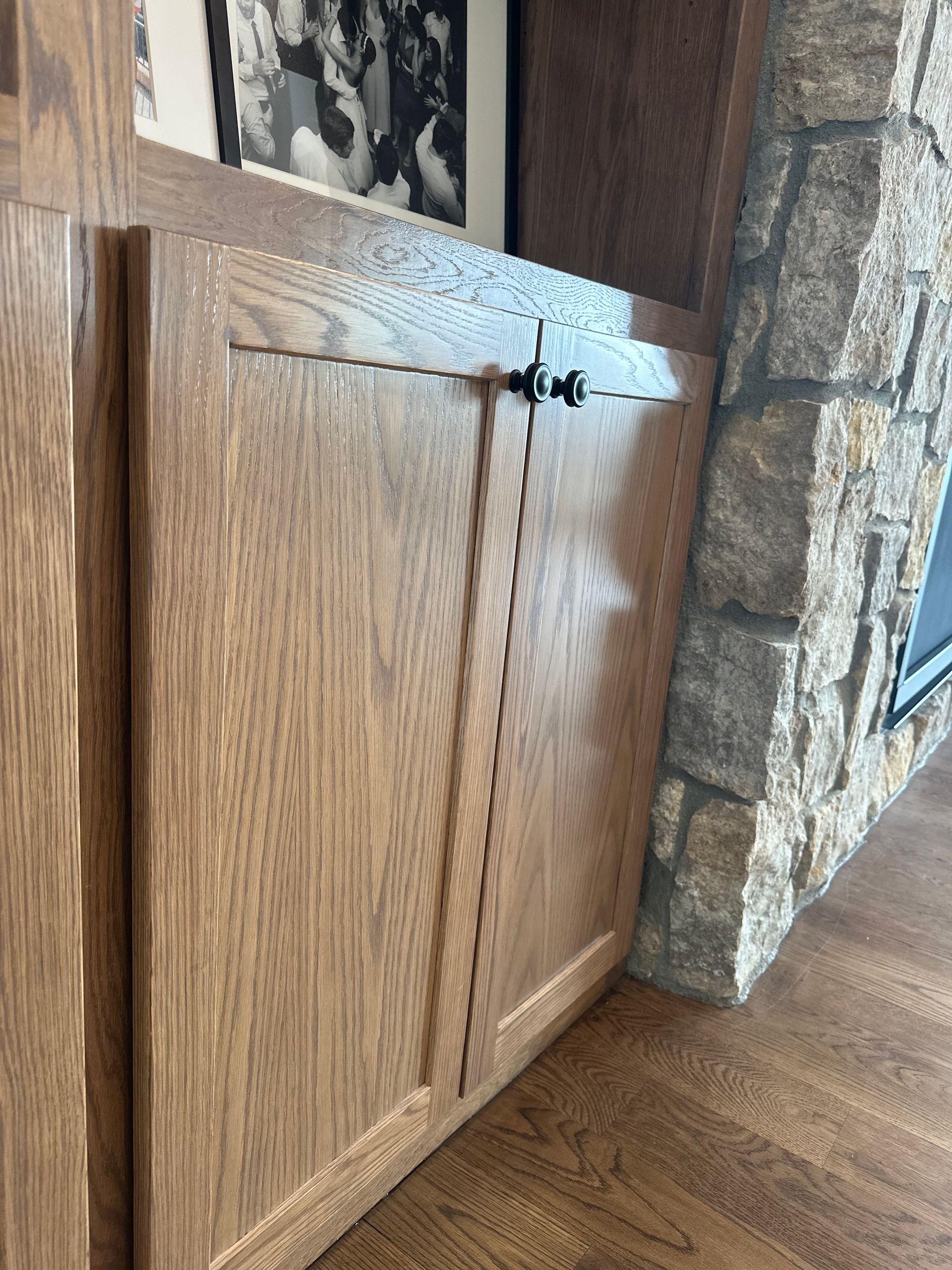 Wooden cabinet with black knobs next to a stone fireplace.