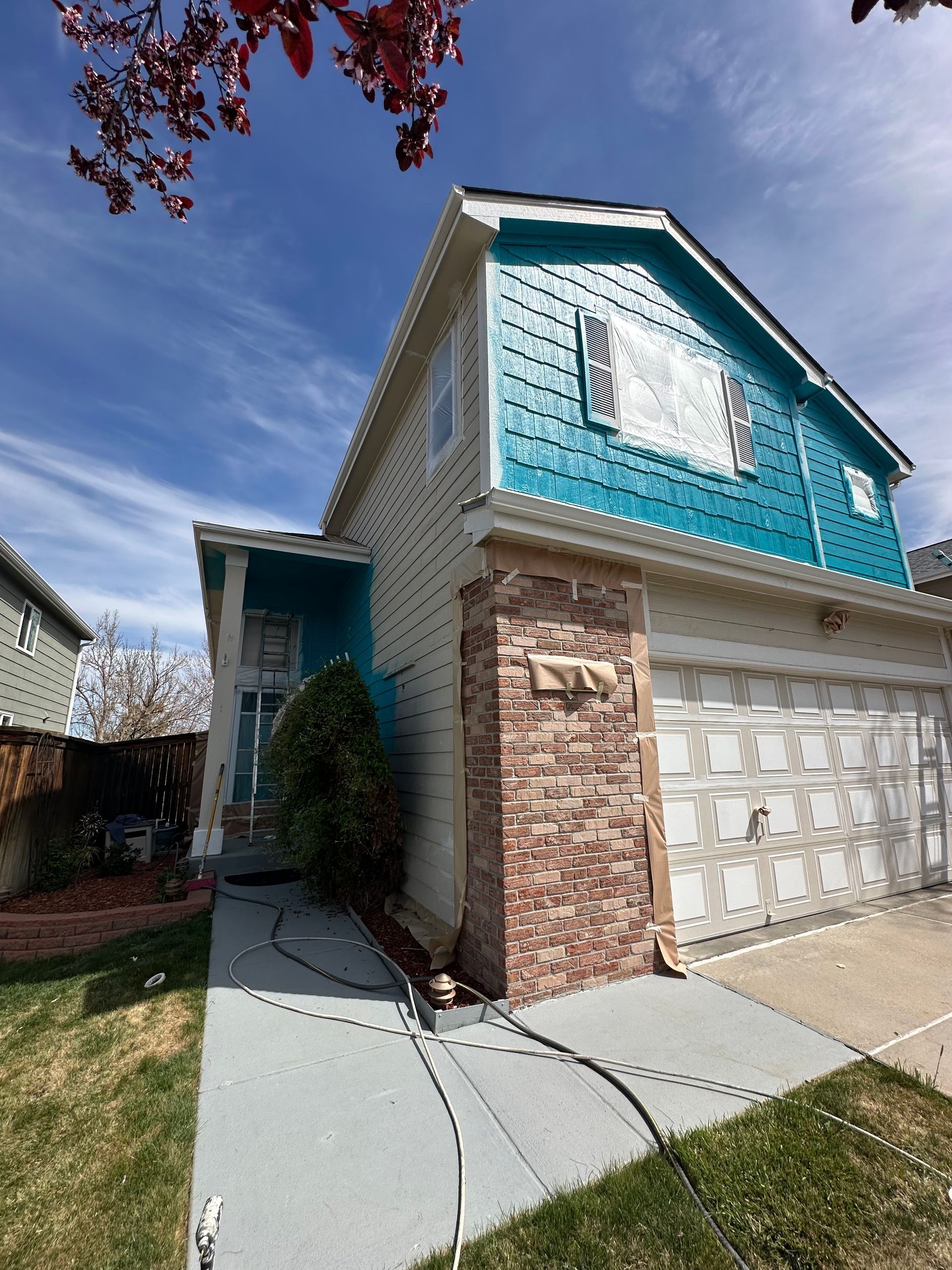 A teal and beige two-story house with a brick facade on the front and a concrete walkway leading to the front door.