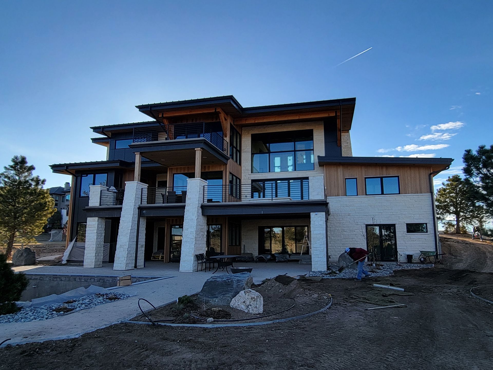 Modern multi-story house with stone columns, large windows, and an expansive patio.