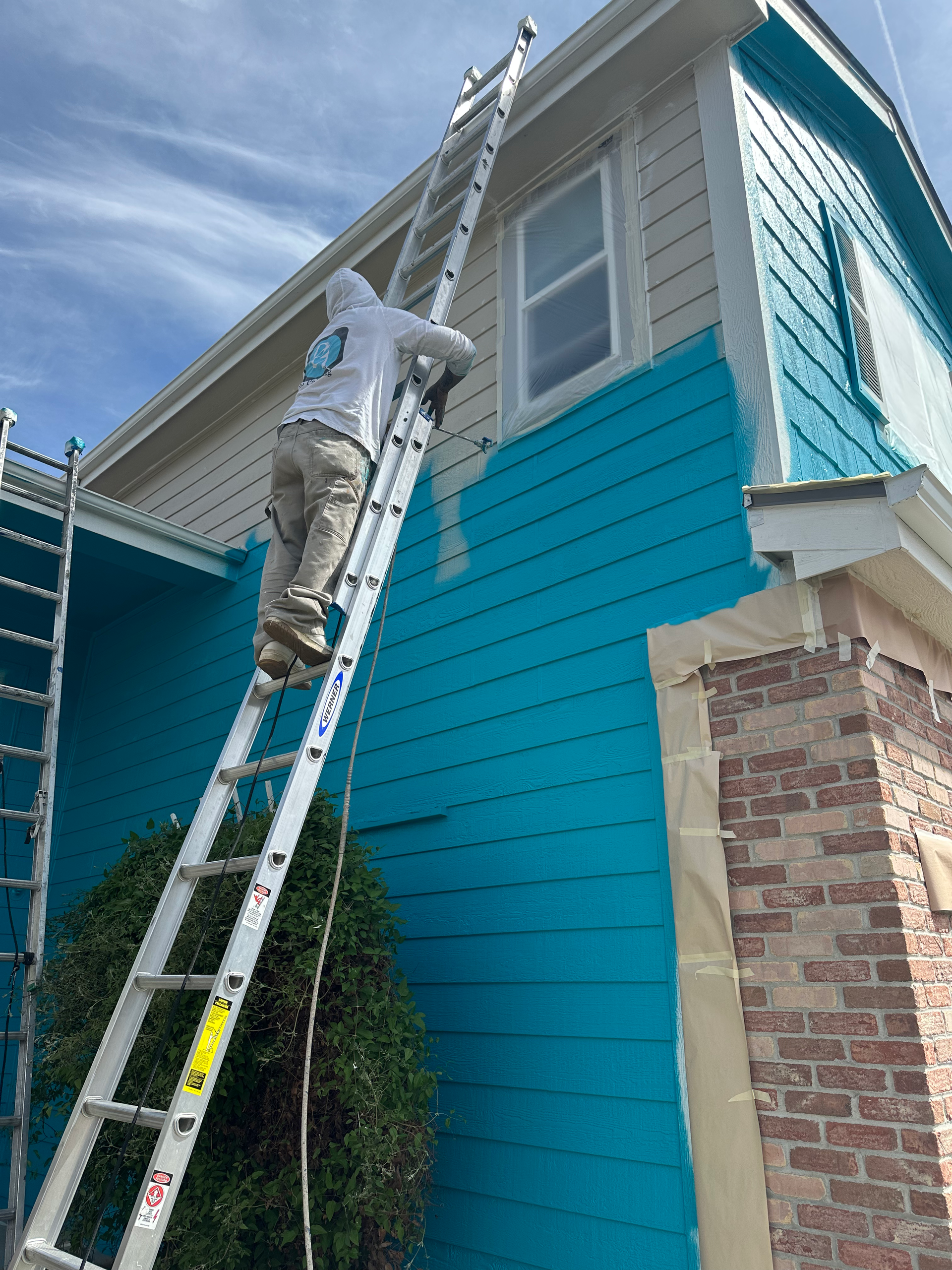A man is painting a blue house with a ladder.