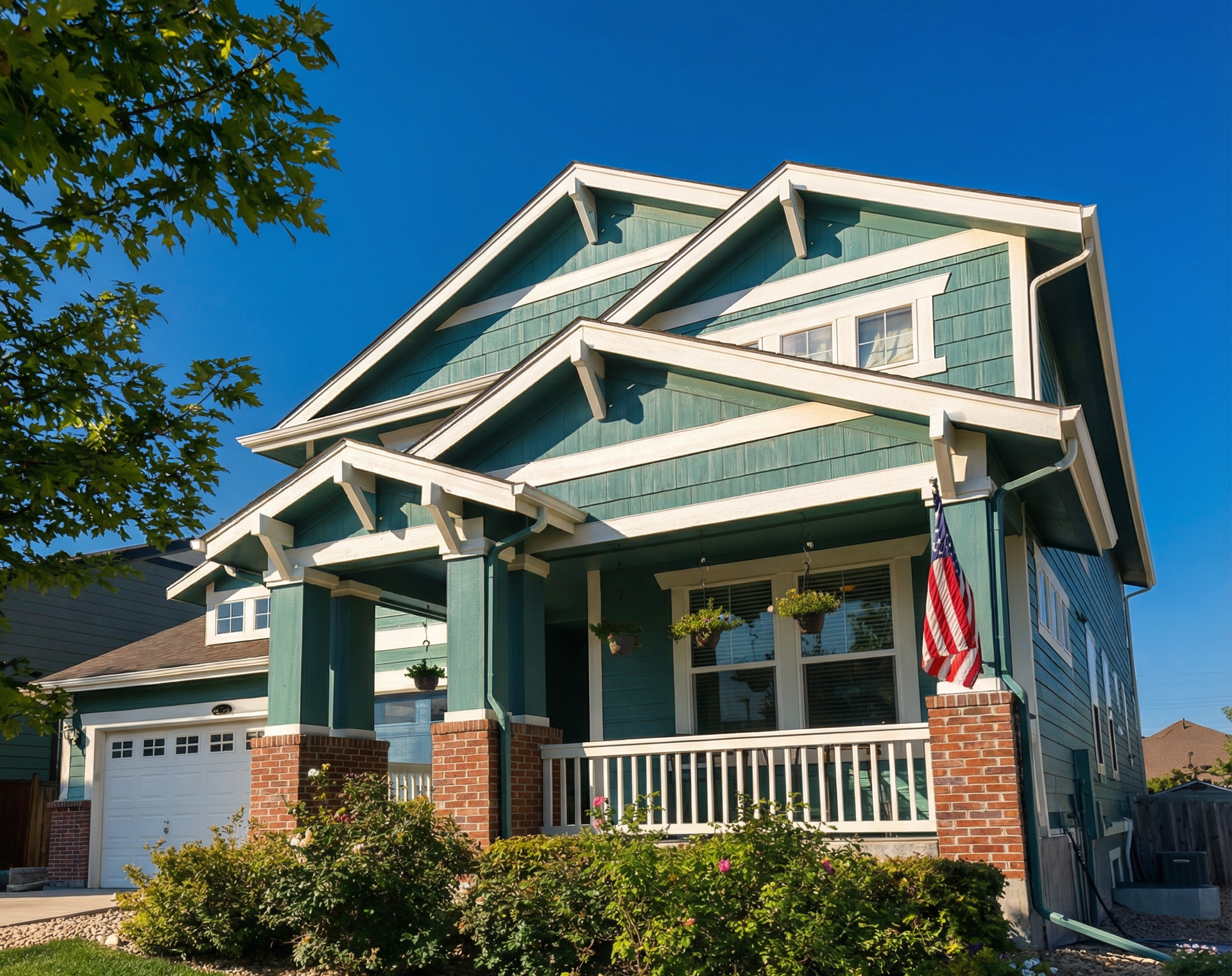 Green house with white trim, red brick accents, and American flag on a sunny day.