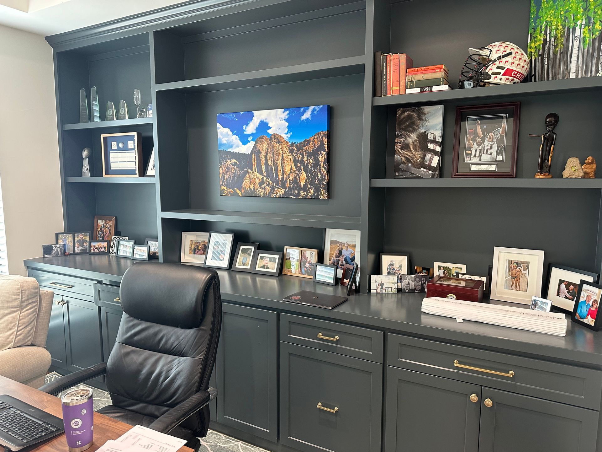 A home office with a desk , chair , shelves and pictures on the wall.