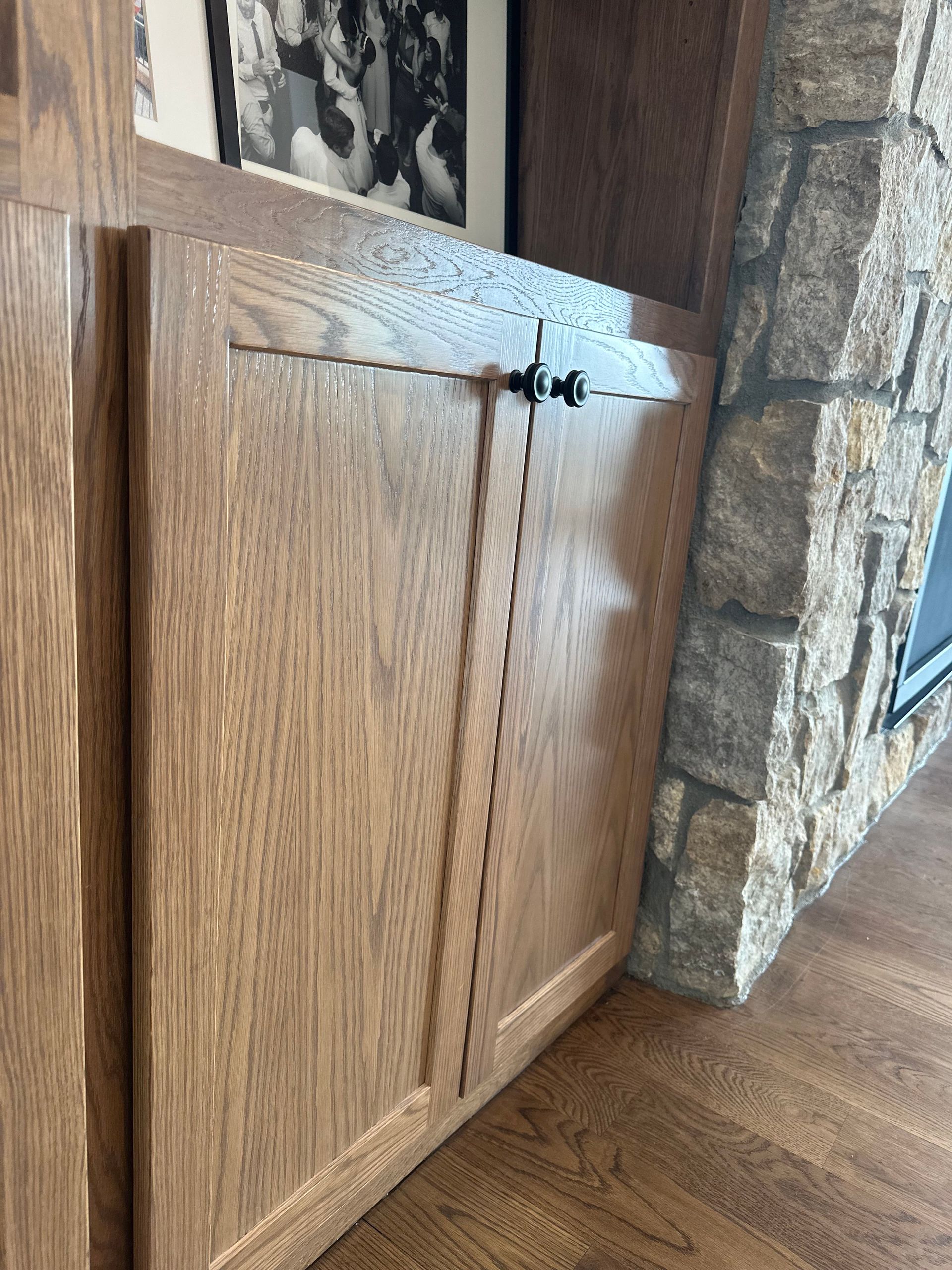A wooden cabinet is next to a stone fireplace in a living room.