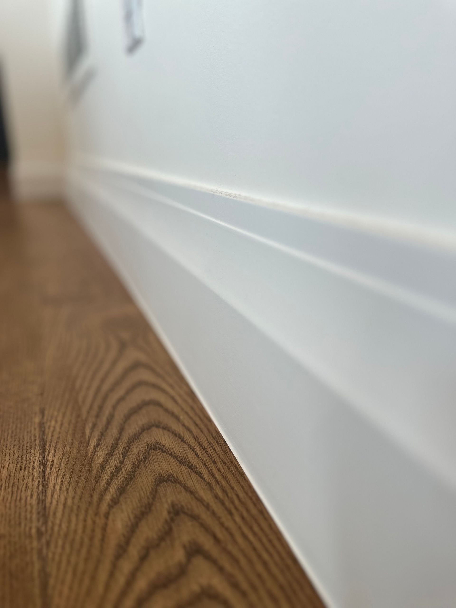 A close up of a white wall with a wooden floor in the background.