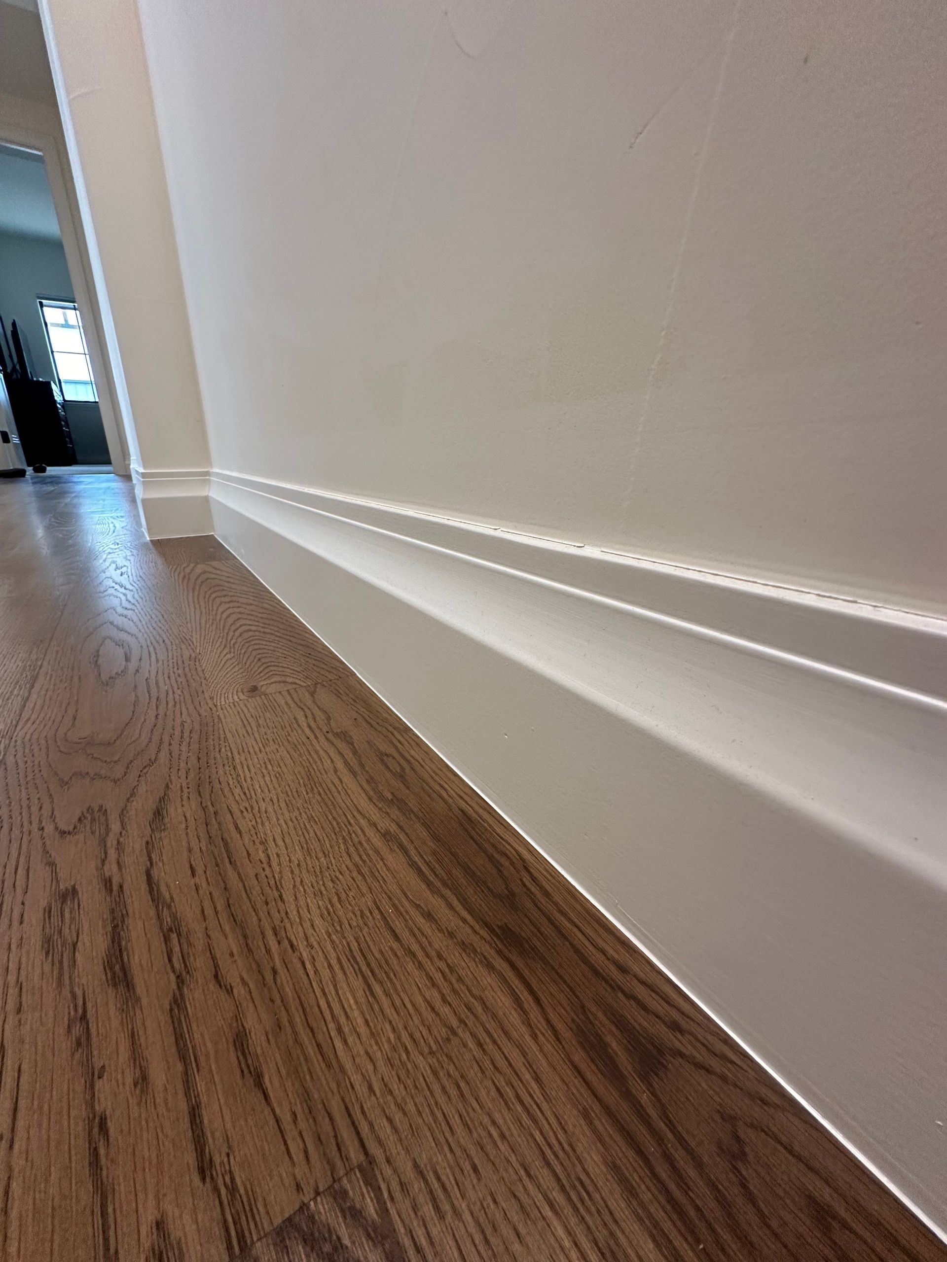 A hallway with a wooden floor and white molding on the wall.