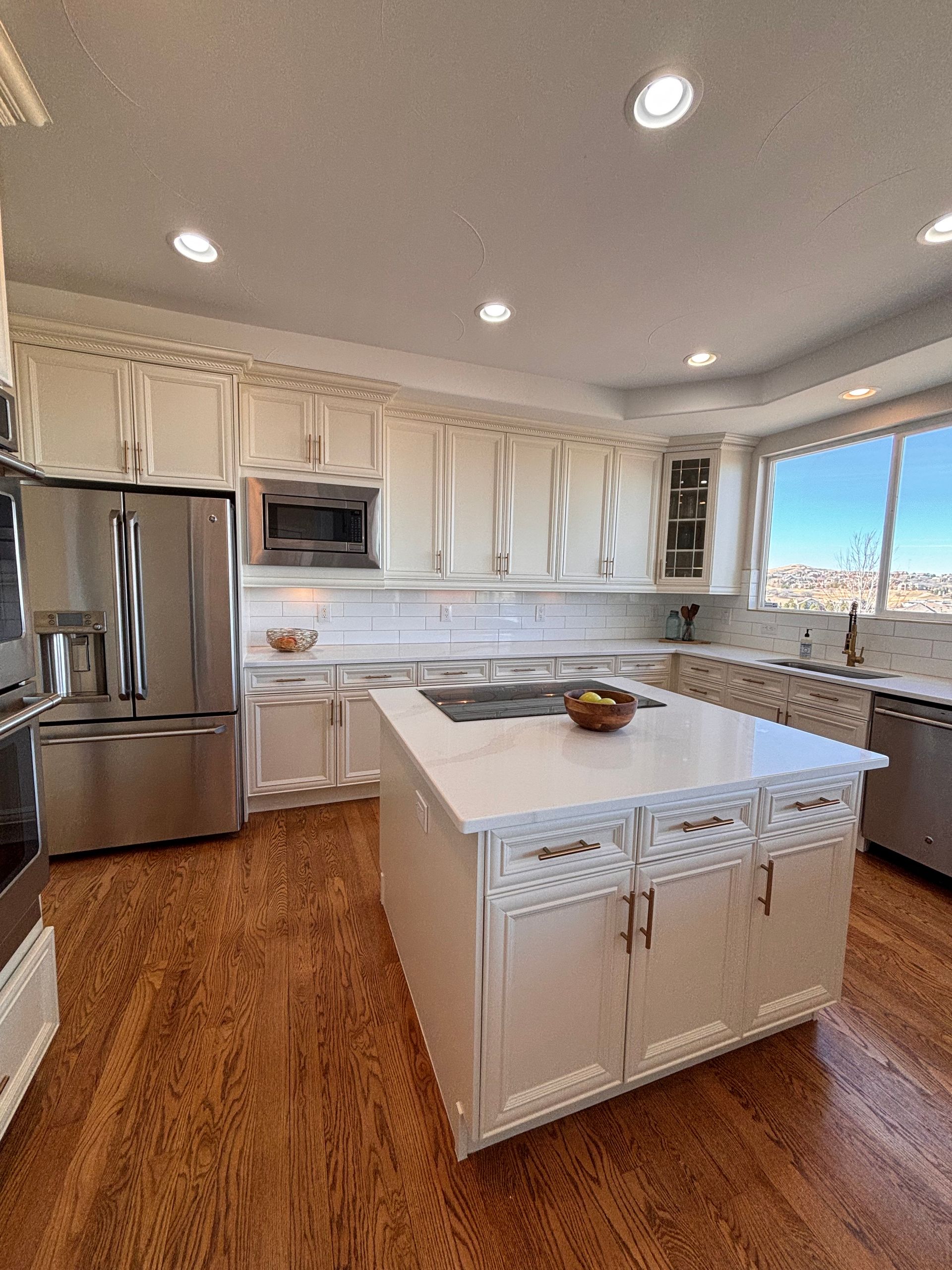 A kitchen with white cabinets, a central island with a stone countertop, stainless steel appliances, and wood flooring.