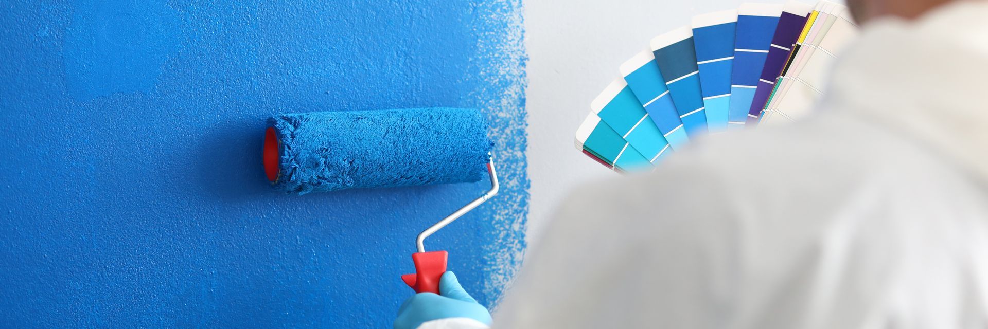 A man is painting a wall with a blue paint roller.