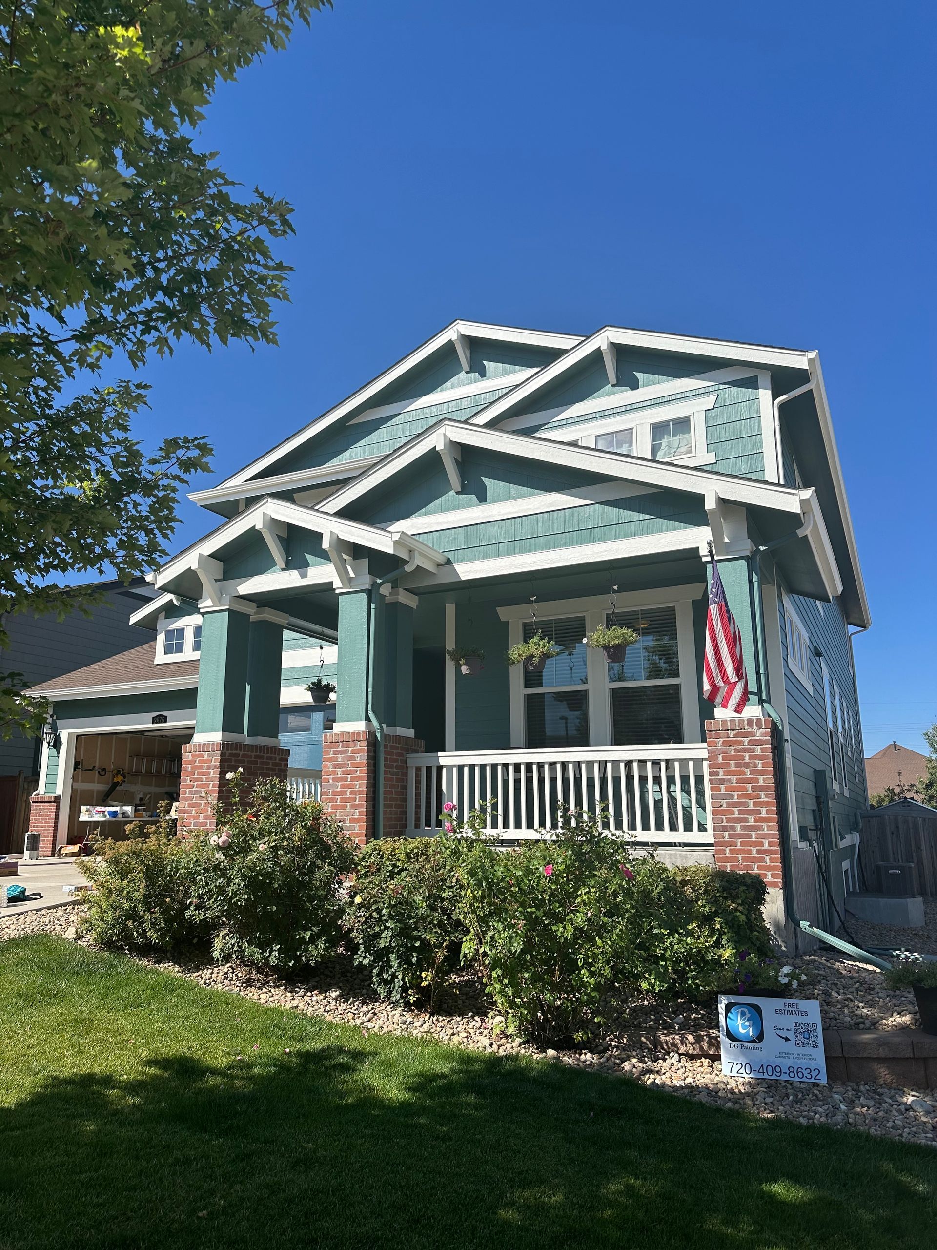 A green house with a white porch and a blue sky in the background.