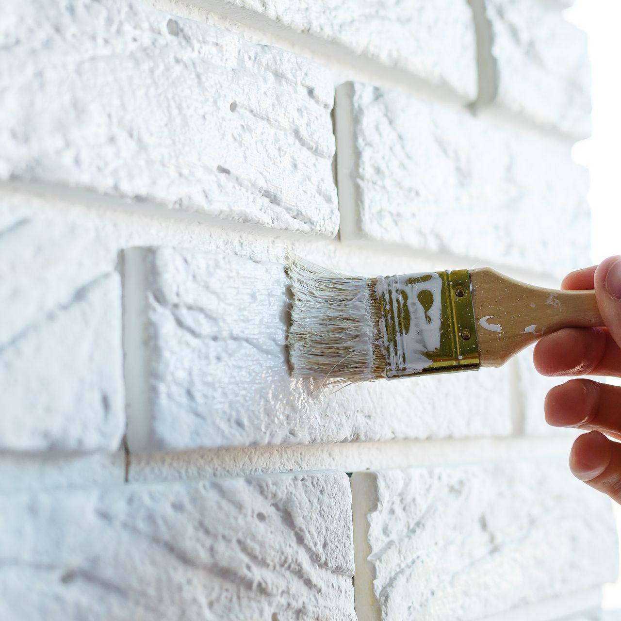 A person is painting a white brick wall with a brush.