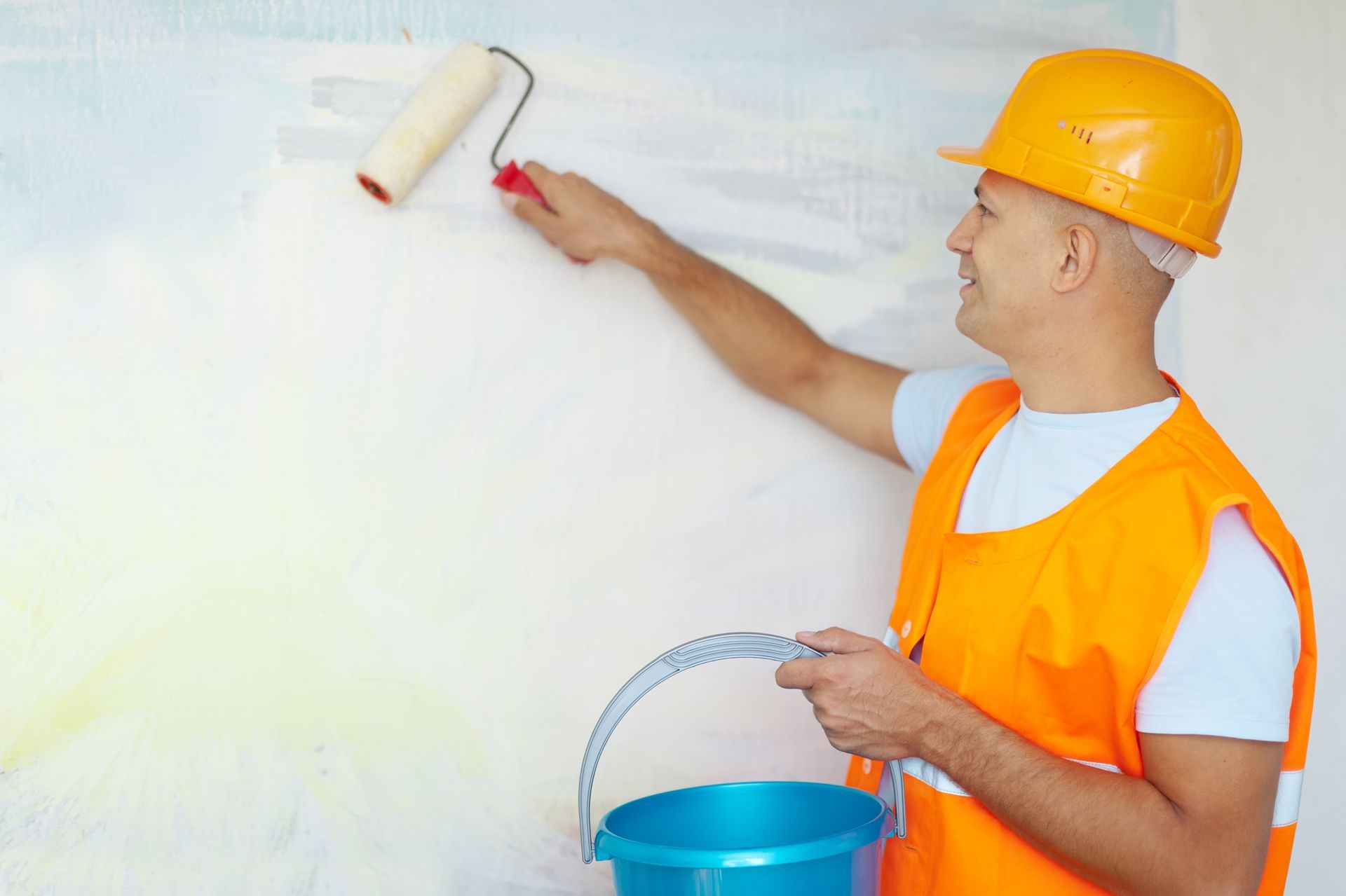 A man is painting a wall with a roller and bucket.