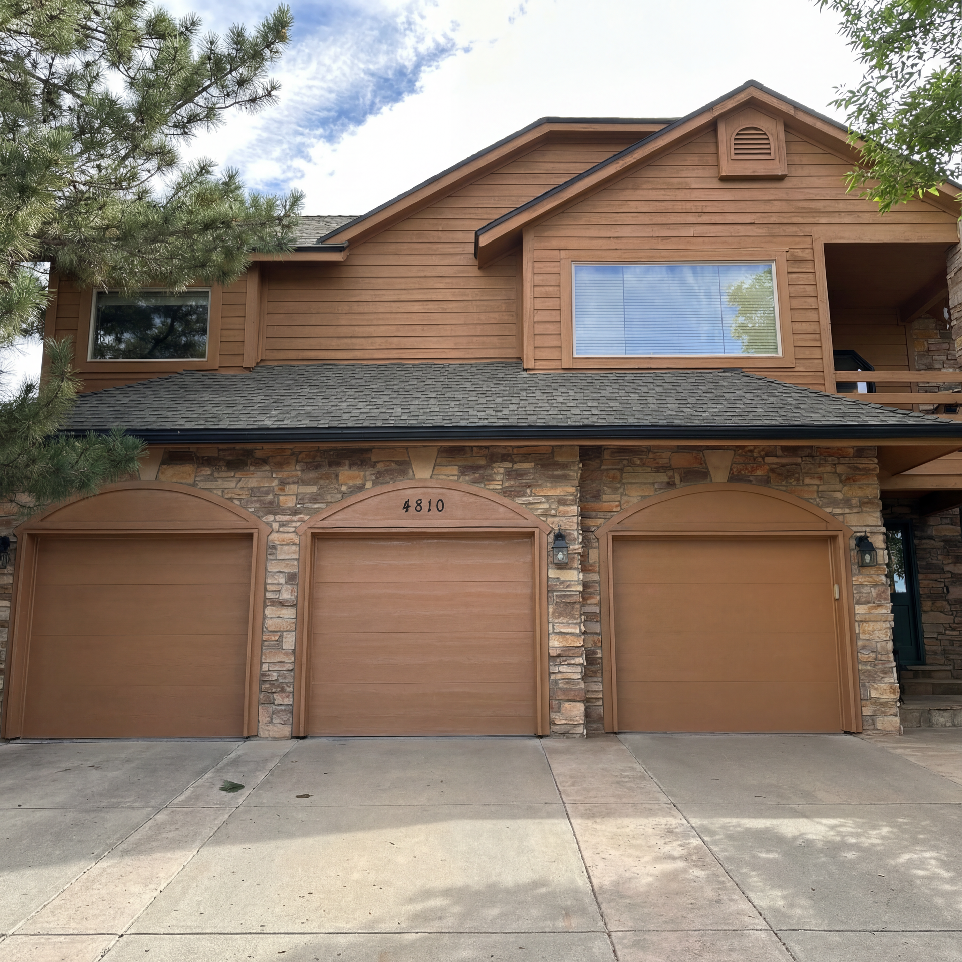 A large house with three garage doors and a jeep parked in front of it.
