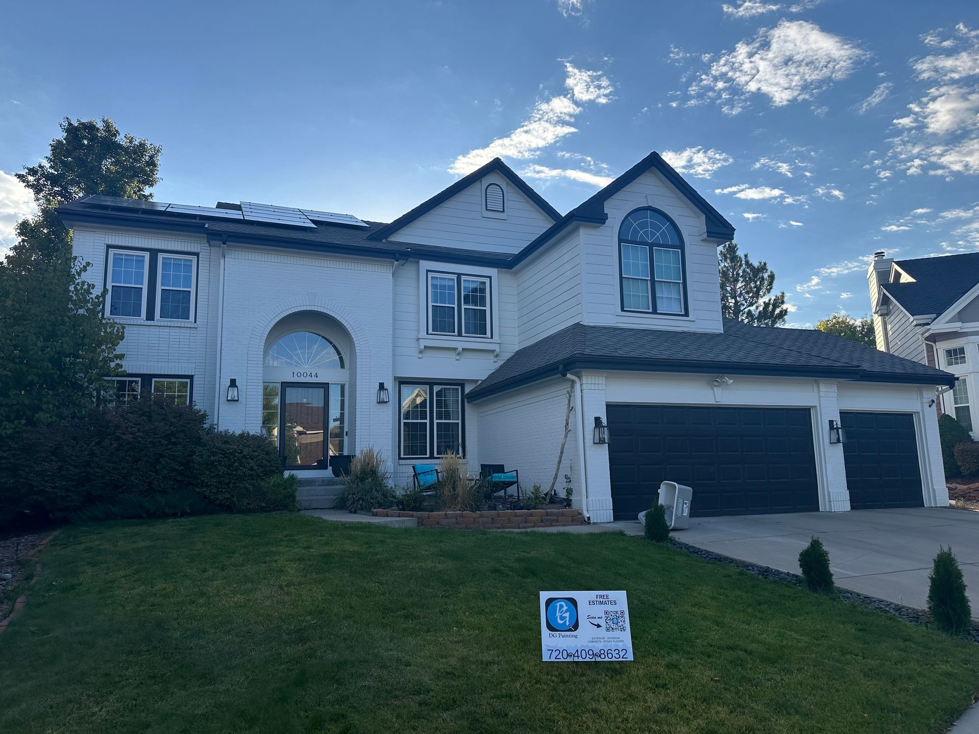 A large white house with black garage doors and a sign in front of it.