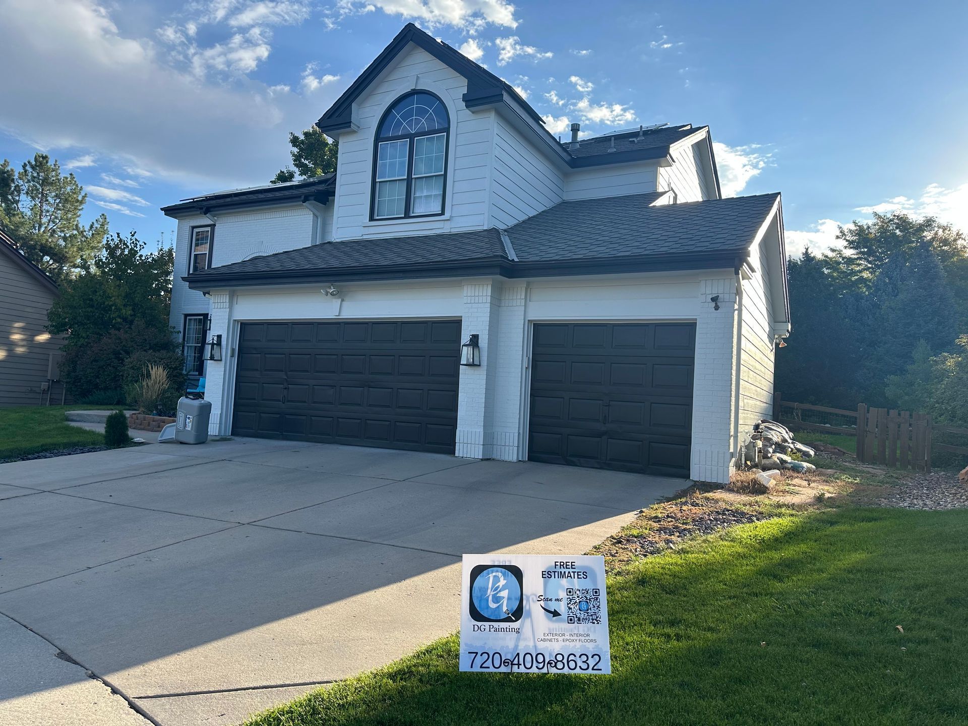 A white house with two garage doors and a sign in front of it.