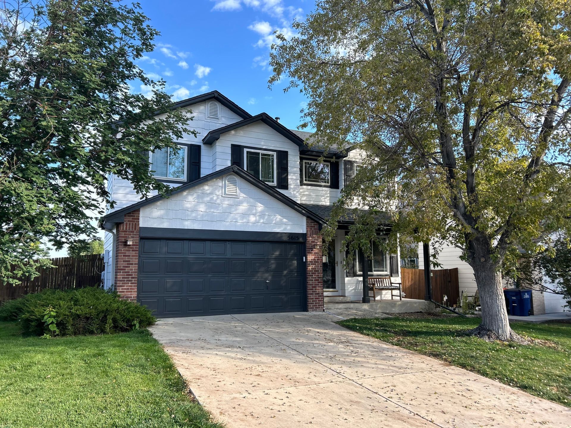 A white house with a black garage door and a tree in front of it.
