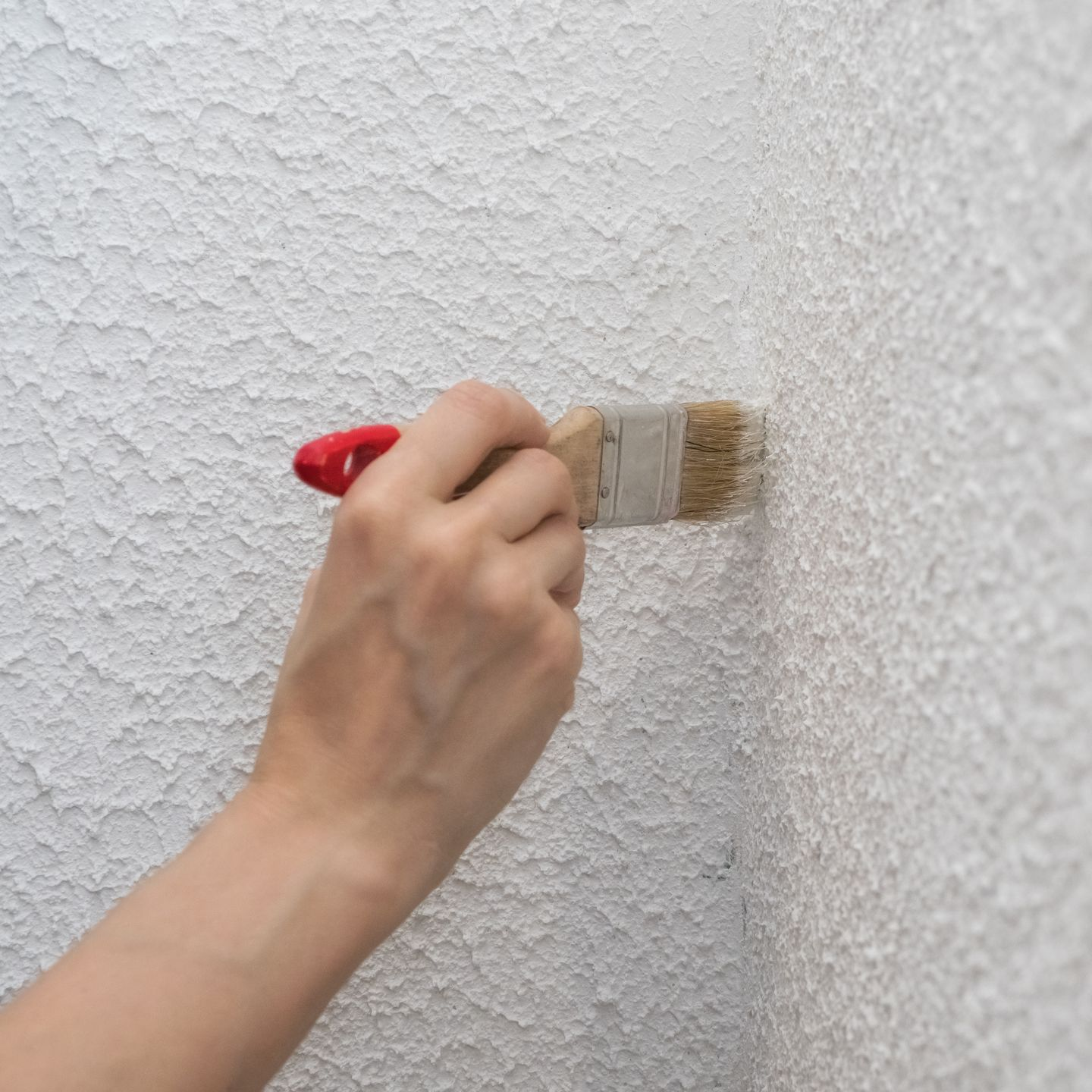 A person is painting a white wall with a brush.