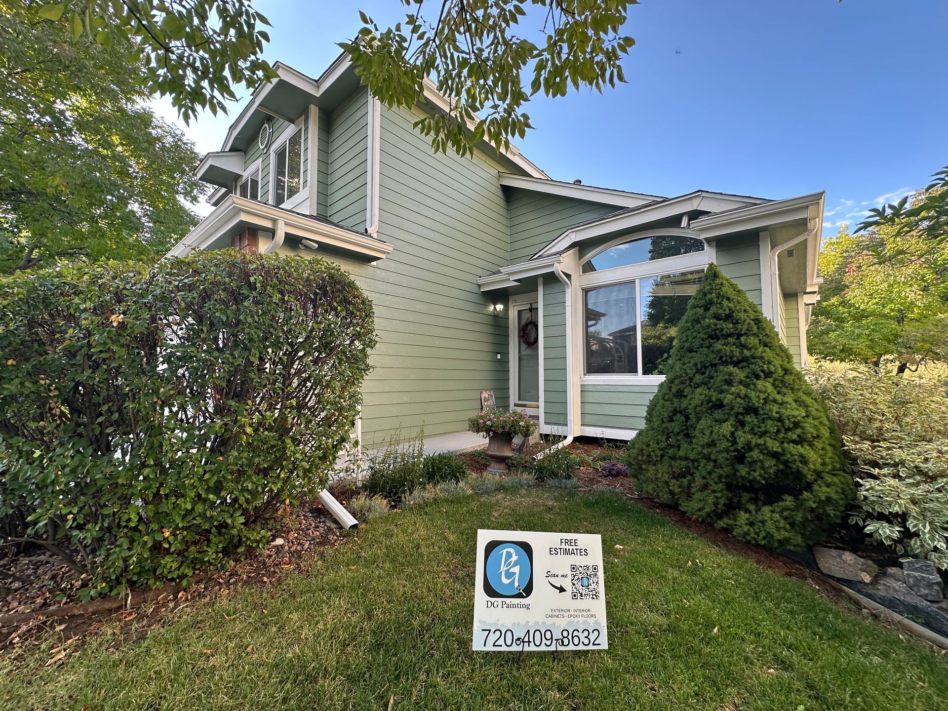 A green house with a for sale sign in front of it.