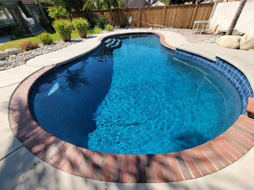 A large swimming pool with blue tiles and a brick border in a backyard.